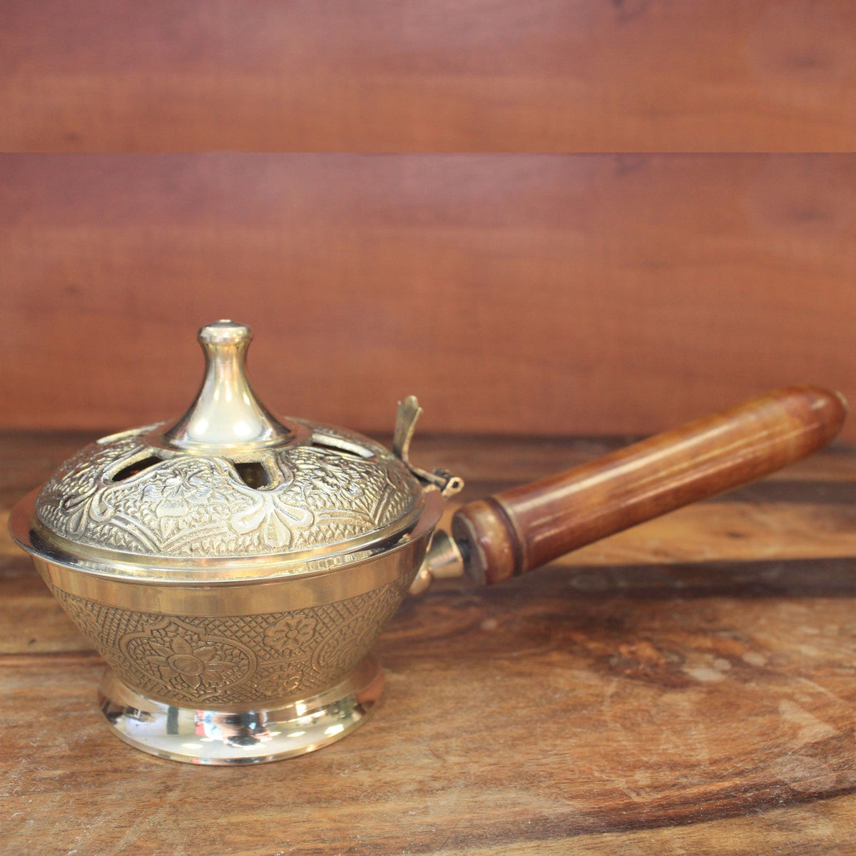 Small Ornate Brass Incense Burner with Handle with a lidded engraved bowl and brown wooden grip on a wood surface by Quintessential Holistic Health Ltd