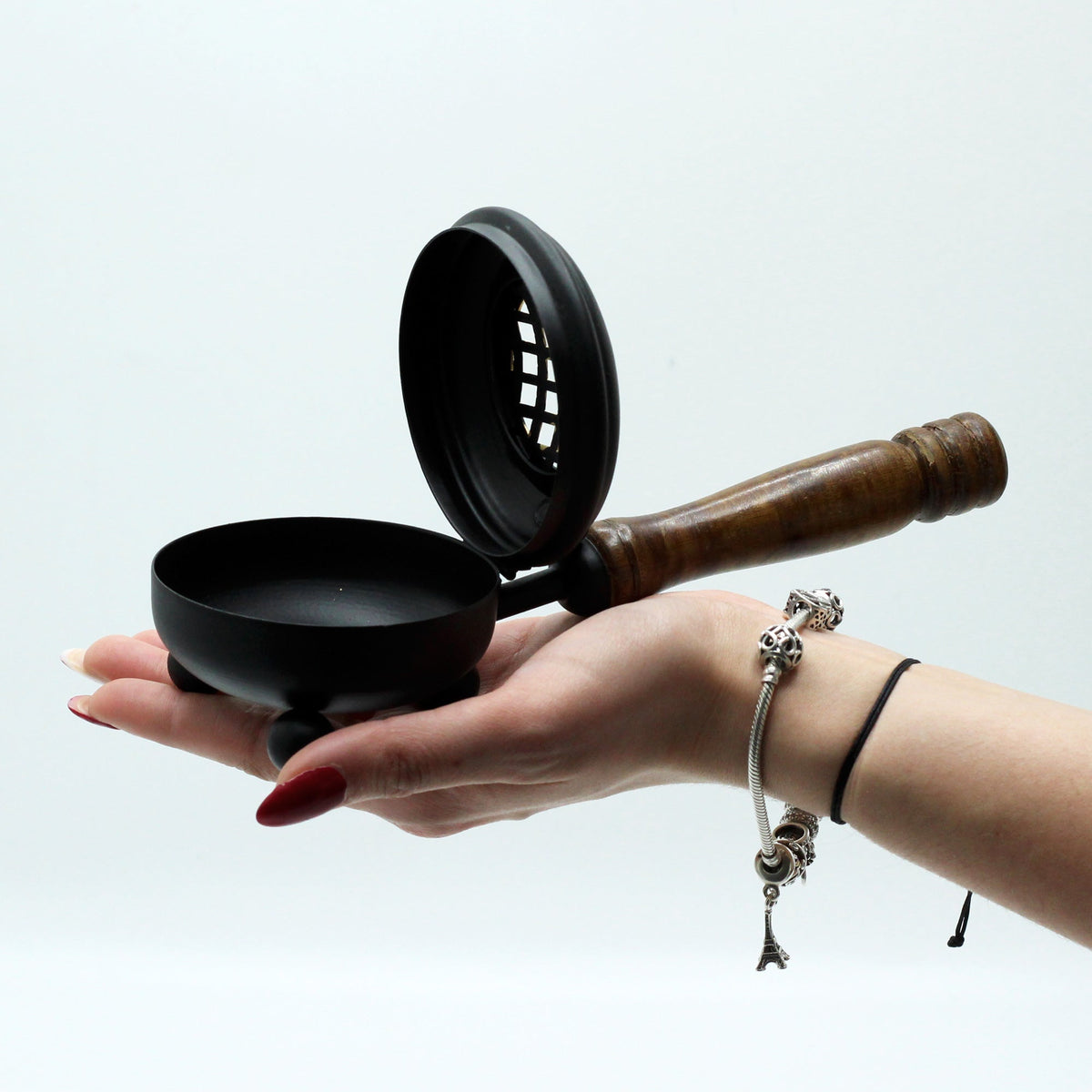 Cast Iron Incense Burner with Gold Detail - Medium shown open and supported on an outstretched hand, with its pierced lid raised by Quintessential Holistic Health Ltd
