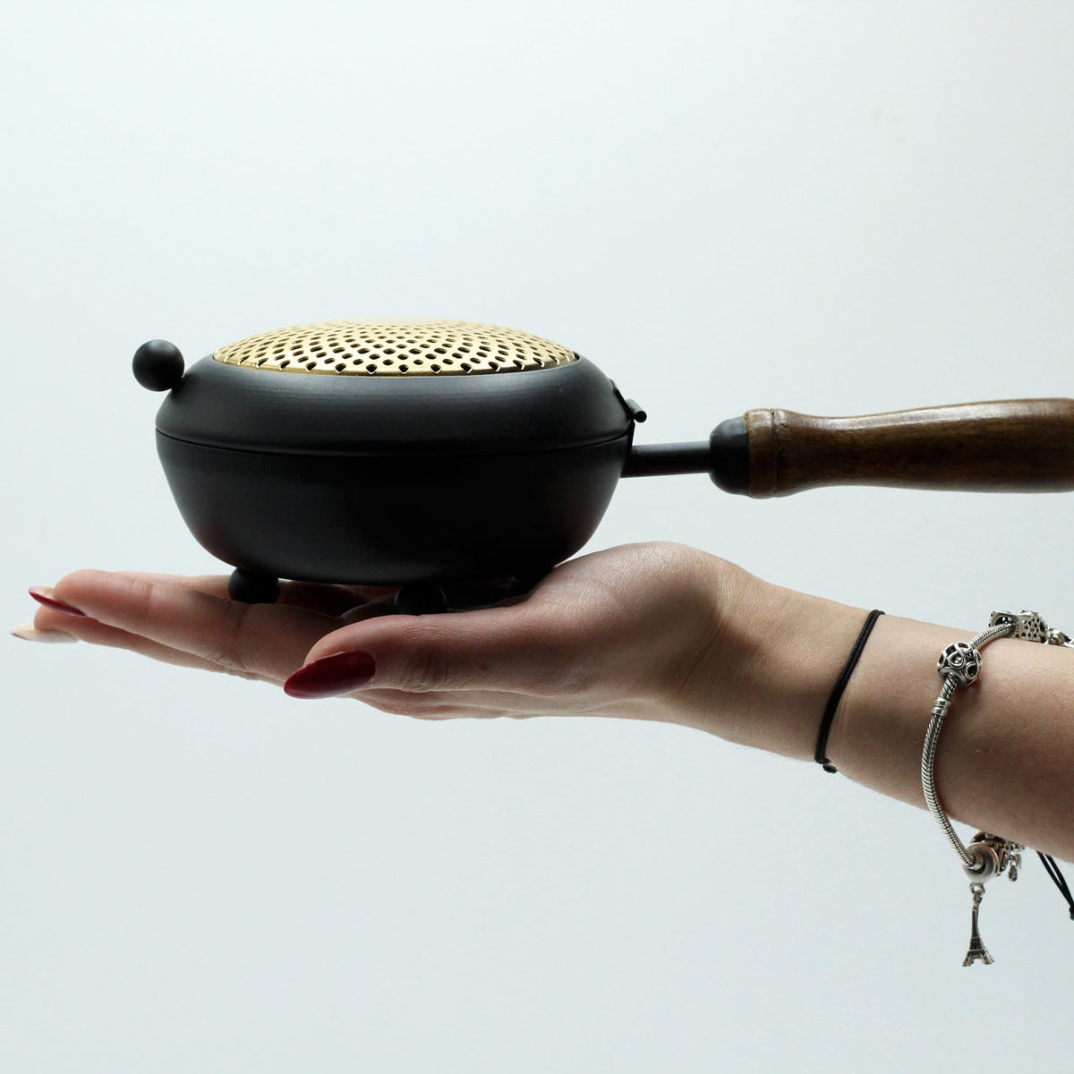 Cast Iron Incense Burner with Gold Detail - Large, with perforated gold lid and wooden side grip, resting on a hand by Quintessential Holistic Health Ltd