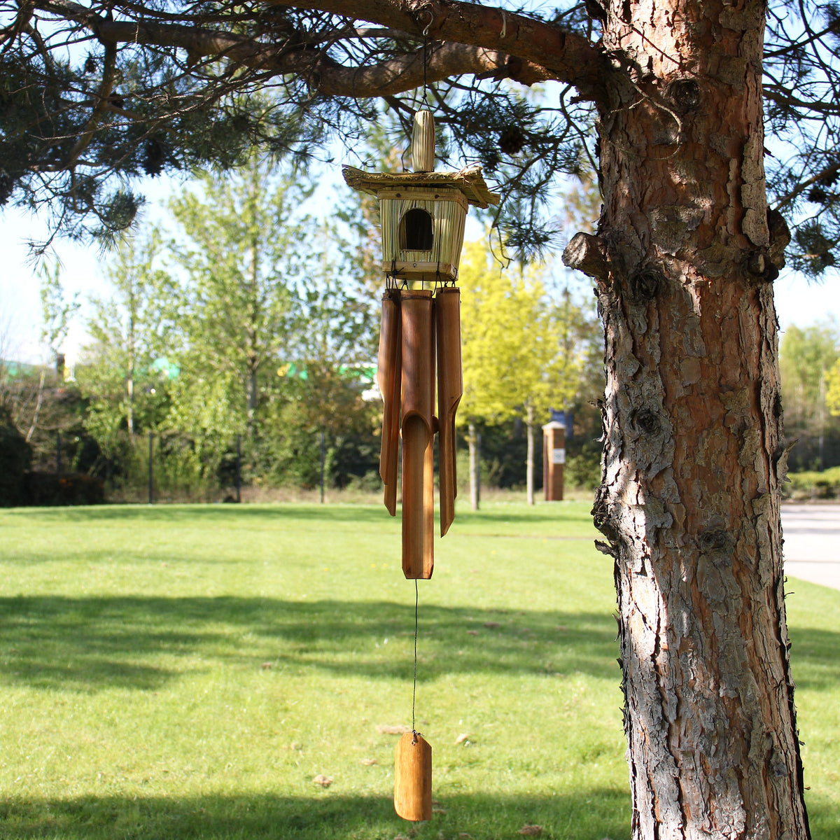 Seagrass & Bamboo Square Bird Box with Chimes - Medium hanging from a tree with a square woven top, four tubes and wooden clapper by Quintessential Holistic Health Ltd