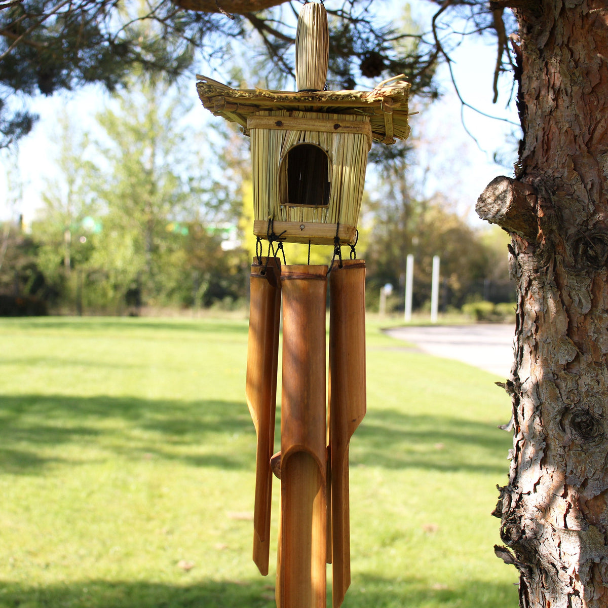 Seagrass & Bamboo Square Bird Box with Chimes - Medium hanging from a tree with four brown tubes and a pale top finial by Quintessential Holistic Health Ltd
