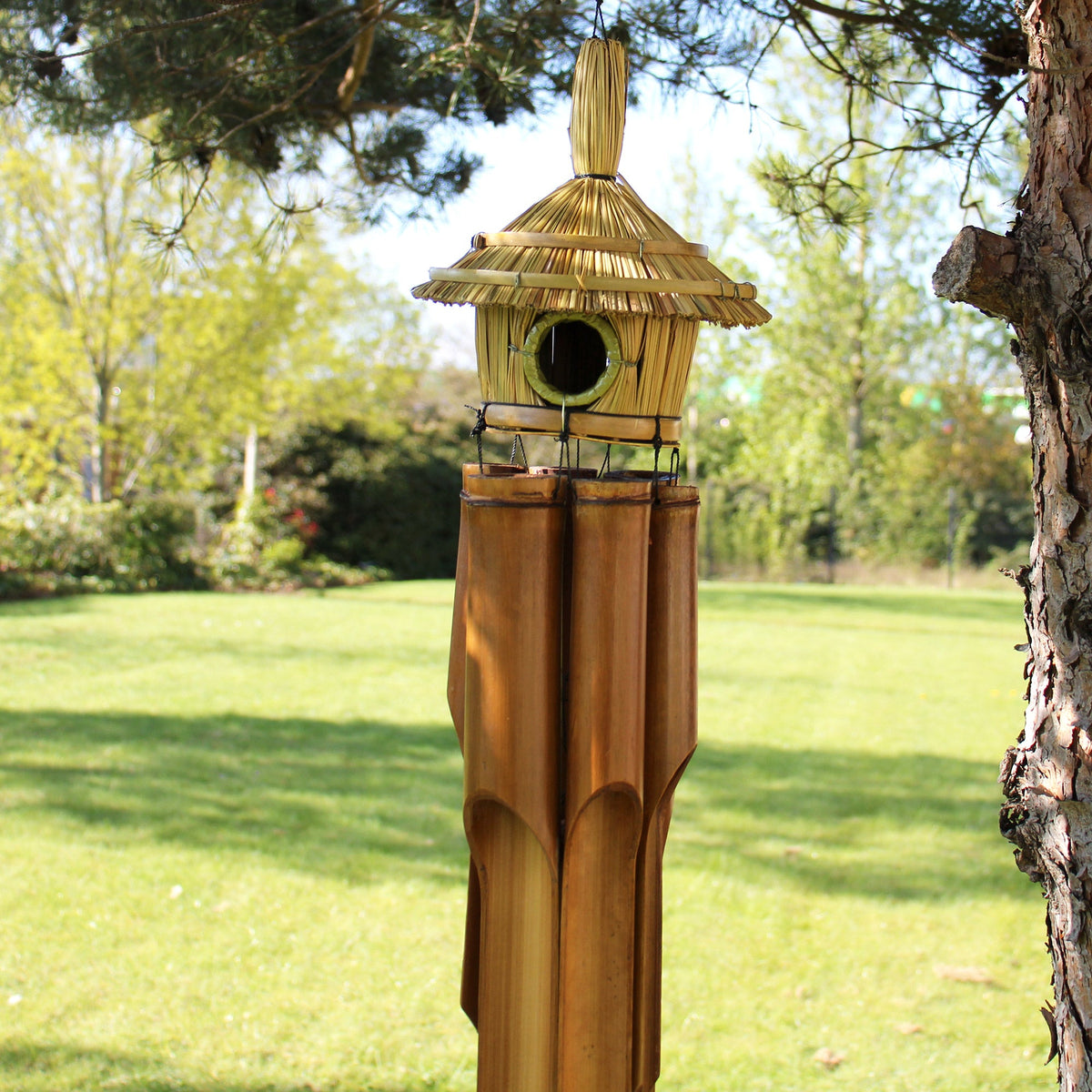Handcrafted Seagrass and Bamboo Wind Chime Bird Box - Large - Round hanging from a tree with pointed roof and long tubes by Quintessential Holistic Health Ltd
