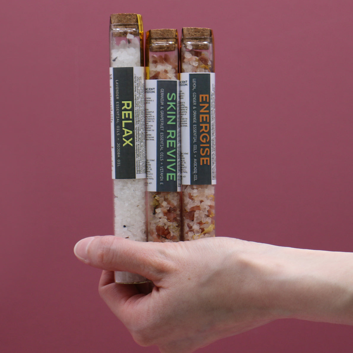 Gift Set of 7 Essential Oil Bath Salts in Vials, with three labelled vials held between two hands, by Quintessential Holistic Health Ltd
