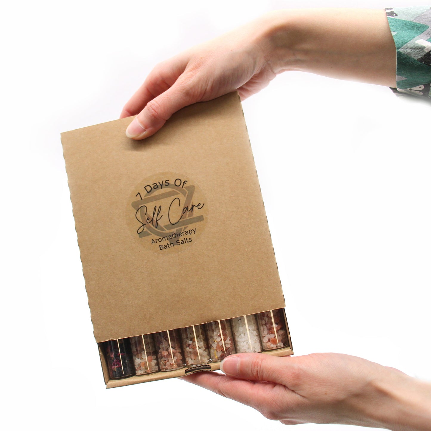 Gift Set of 7 Essential Oil Bath Salts in Vials, shown in a cardboard sleeve held by two hands, by Quintessential Holistic Health Ltd