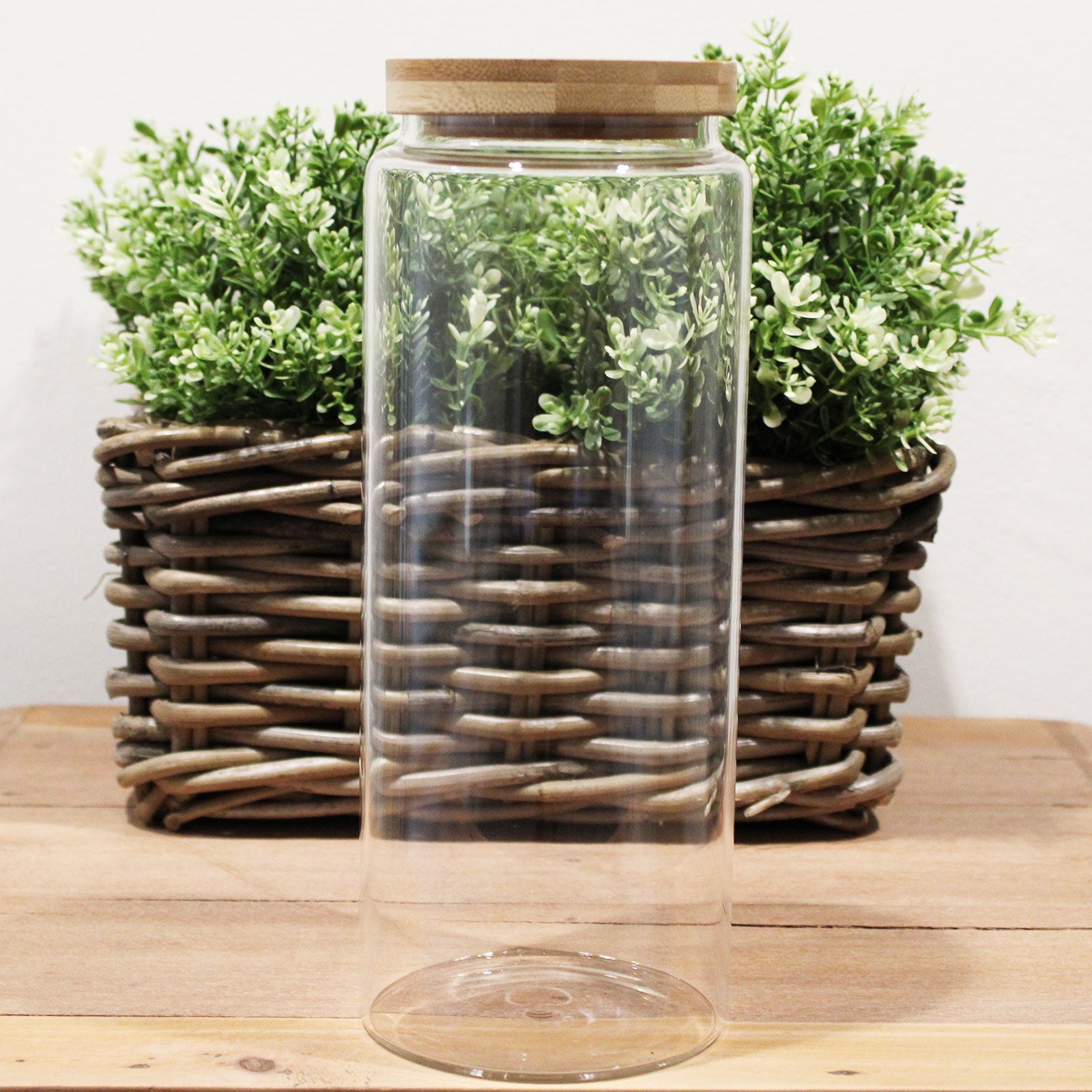 Cottage Bamboo Glass Jar with Bamboo Lid - 25 cm, tall empty clear jar standing before a woven planter of green foliage by Quintessential Holistic Health Ltd
