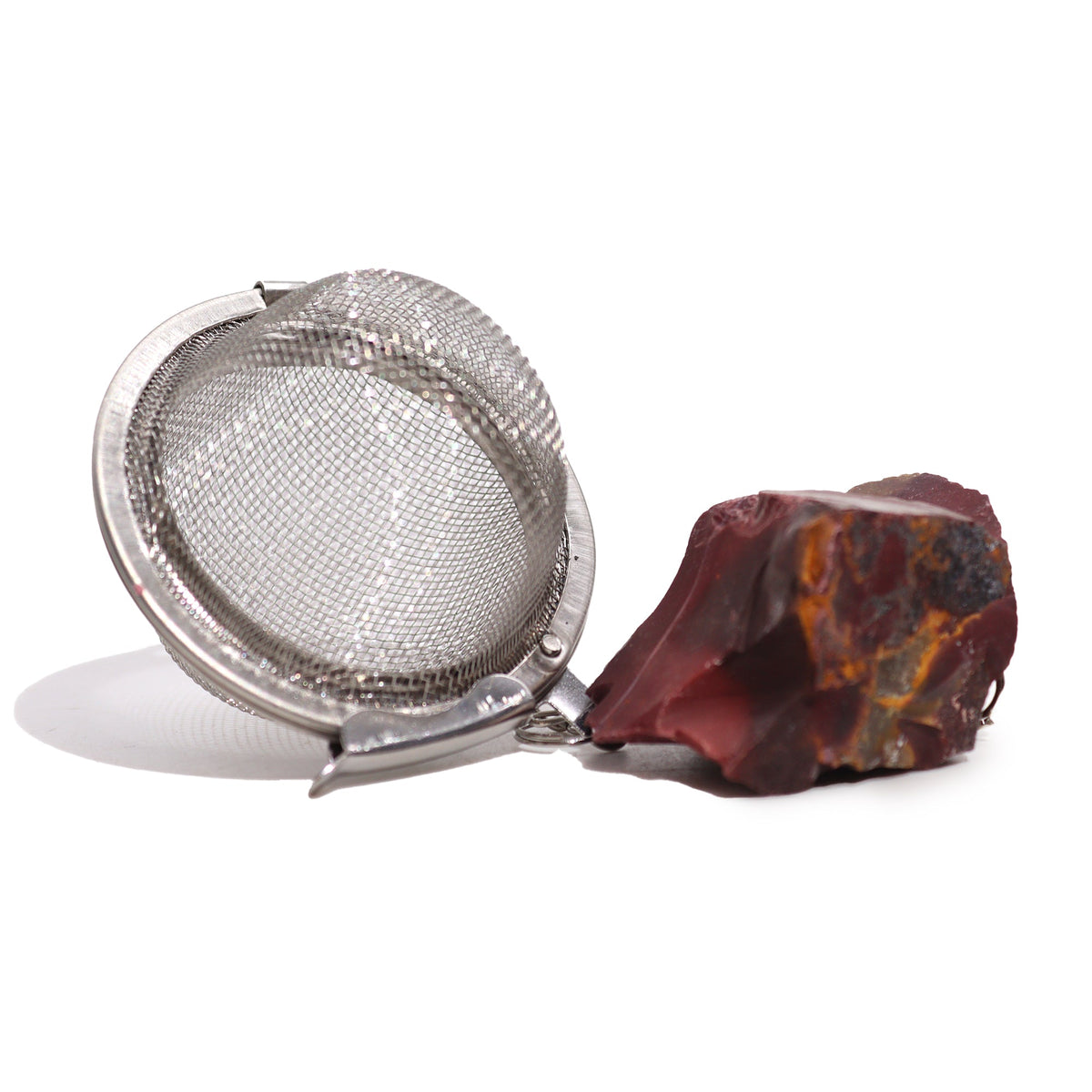 Raw Crystal Gemstone Tea Strainer – Mookaite, Creativity with an open silver mesh ball beside a large mottled red-brown stone by Quintessential Holistic Health Ltd