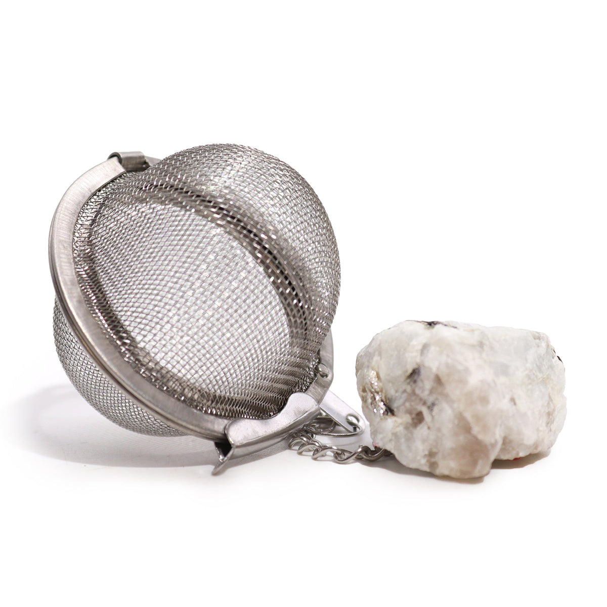 Raw Crystal Gemstone Tea Strainer – Rainbow Moonstone, Empowerment with an open silver mesh ball beside a large rough white stone by Quintessential Holistic Health Ltd