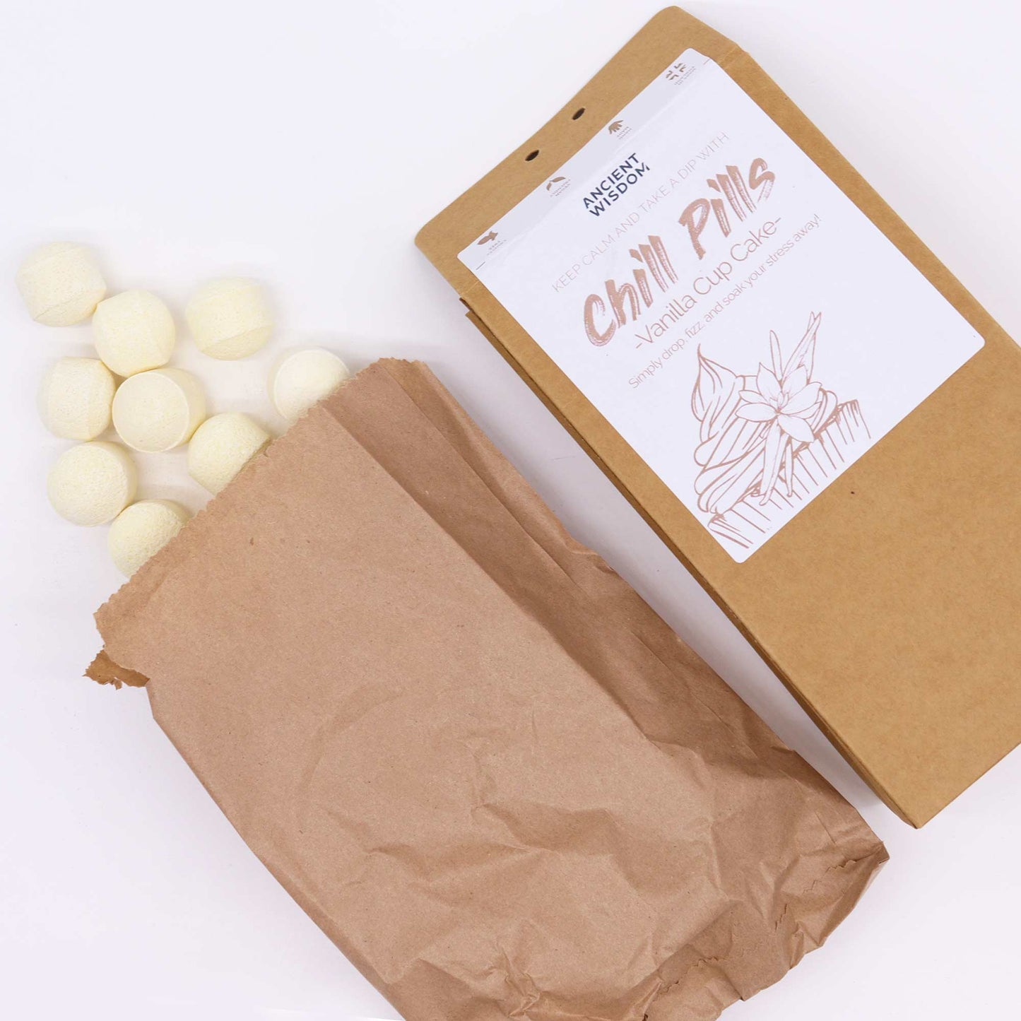 Bath Bomb Chill Pills Gift Pack - Vanilla Cup Cake - 350g, angled brown box with an open paper bag and scattered pale yellow balls by Quintessential Holistic Health Ltd