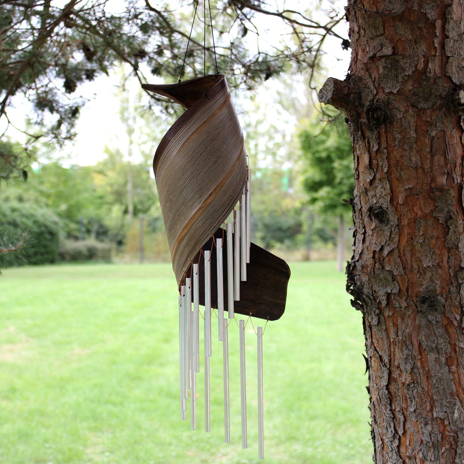 Handcrafted Coconut Leaf Wind Chime - Natural hanging beside a tree with a warm brown spiral leaf and silver-tone tubes by Quintessential Holistic Health Ltd