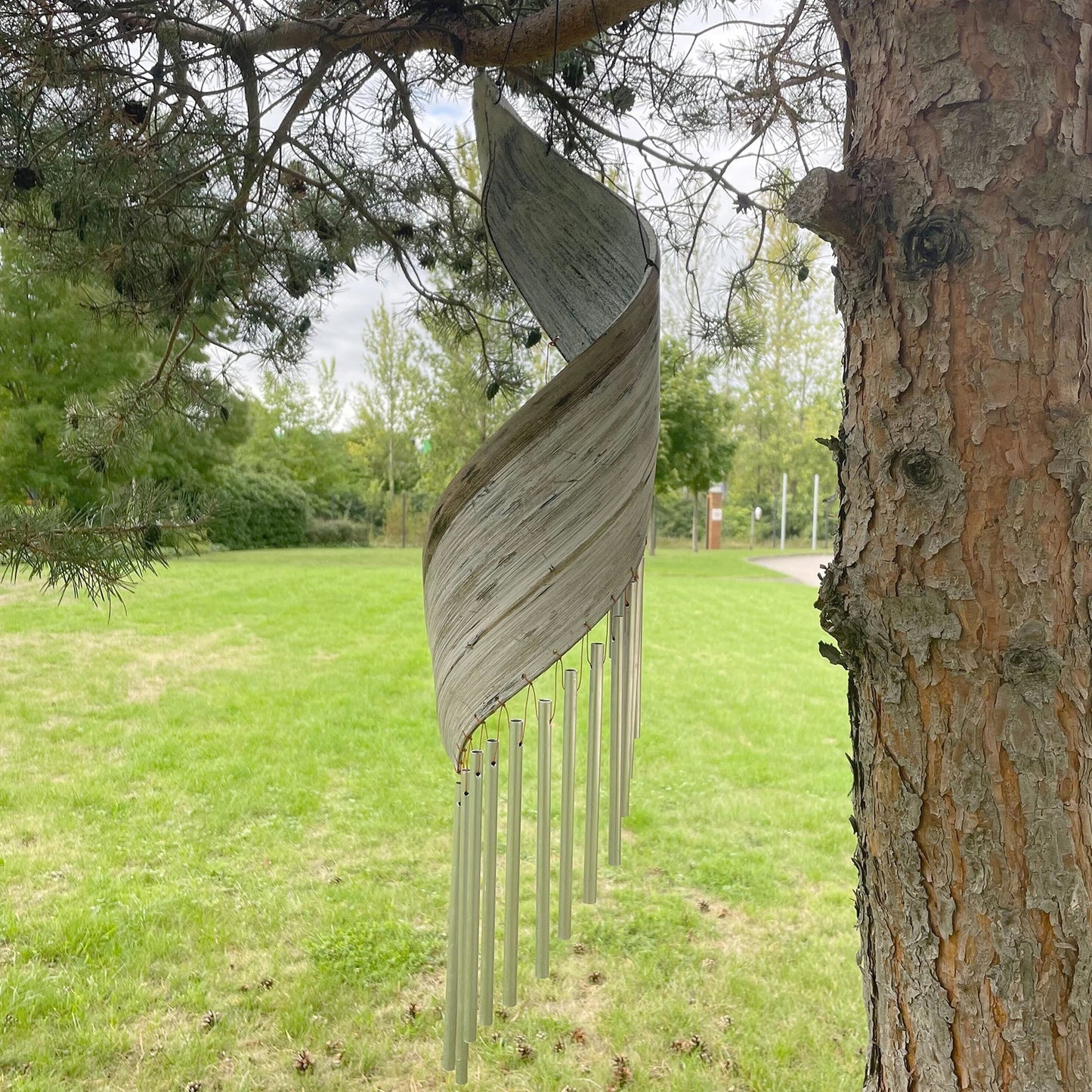 Handcrafted Coconut Leaf Wind Chime - Whitewash hanging near a tree with overlapping pale leaf panels and silver-tone tubes by Quintessential Holistic Health Ltd