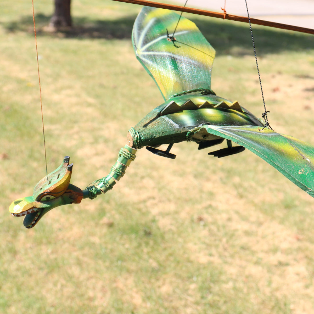 Handcrafted Green Coconut Shell Dragon Mobile - 37cm shown outdoors with spread wings, arched neck and colourful head by Quintessential Holistic Health Ltd