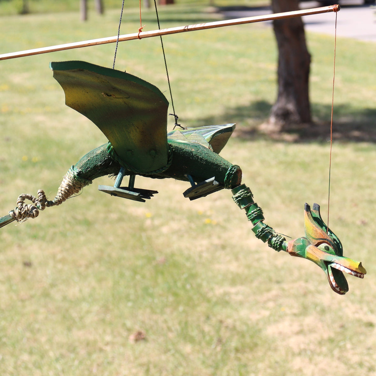 Handcrafted Green Coconut Shell Dragon Mobile - 37cm shown in profile outdoors with raised wings and a long jointed body by Quintessential Holistic Health Ltd