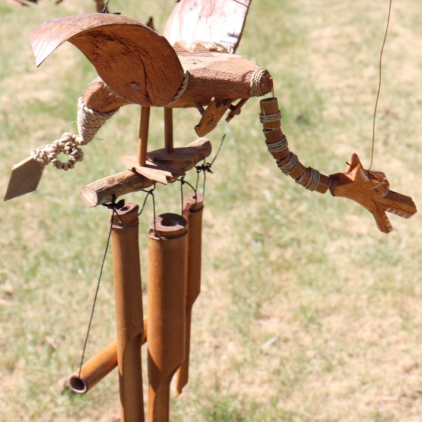 Handcrafted Coconut Shell Wind Chime - Dragon, brown dragon with spread wings above hanging tubes outdoors by Quintessential Holistic Health Ltd