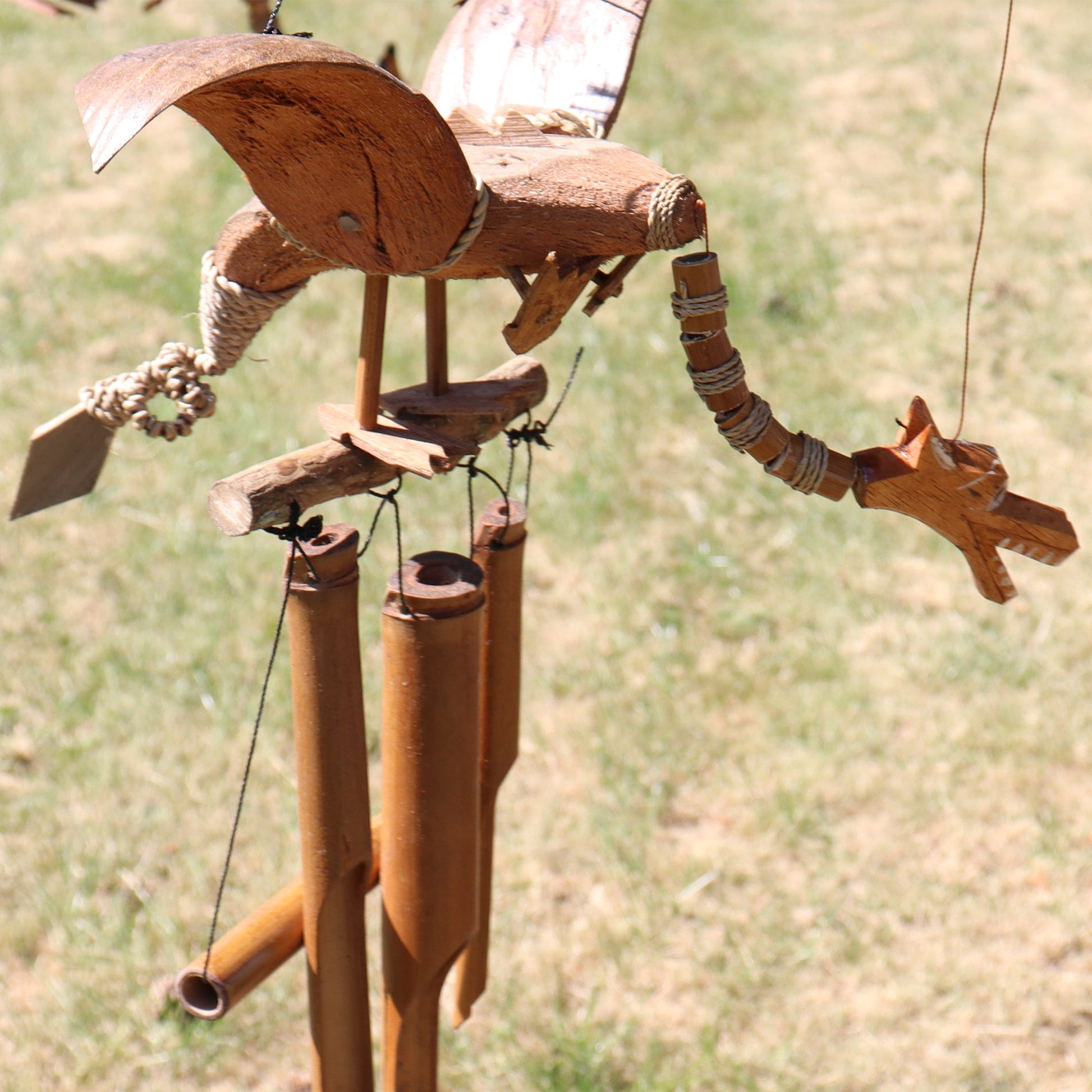 Handcrafted Coconut Shell Wind Chime - Dragon, brown dragon with spread wings above hanging tubes outdoors by Quintessential Holistic Health Ltd