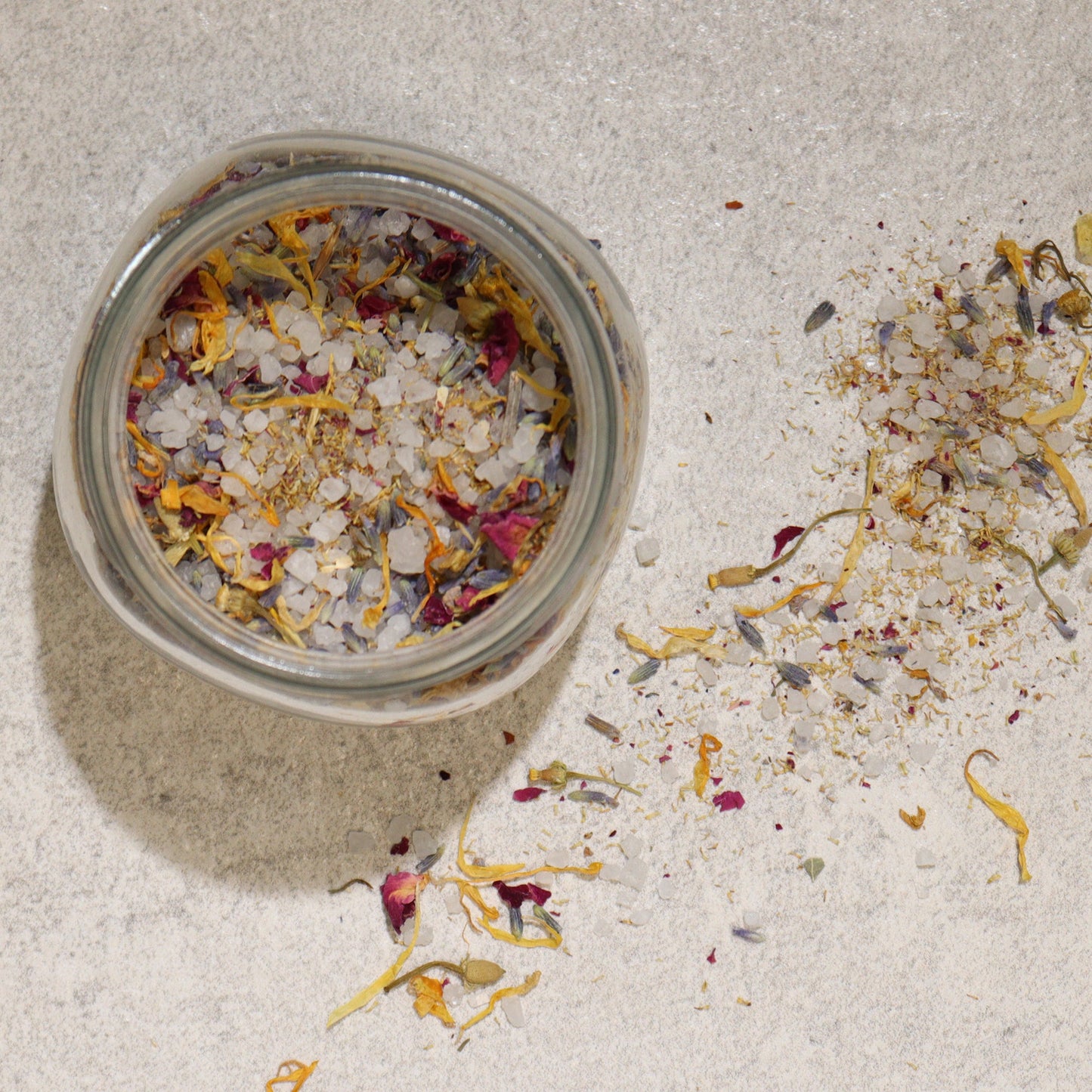 Natural Floral Bath Soak - 140g, open glass jar beside a loose pile of pale crystals and dried petals, by Quintessential Holistic Health Ltd