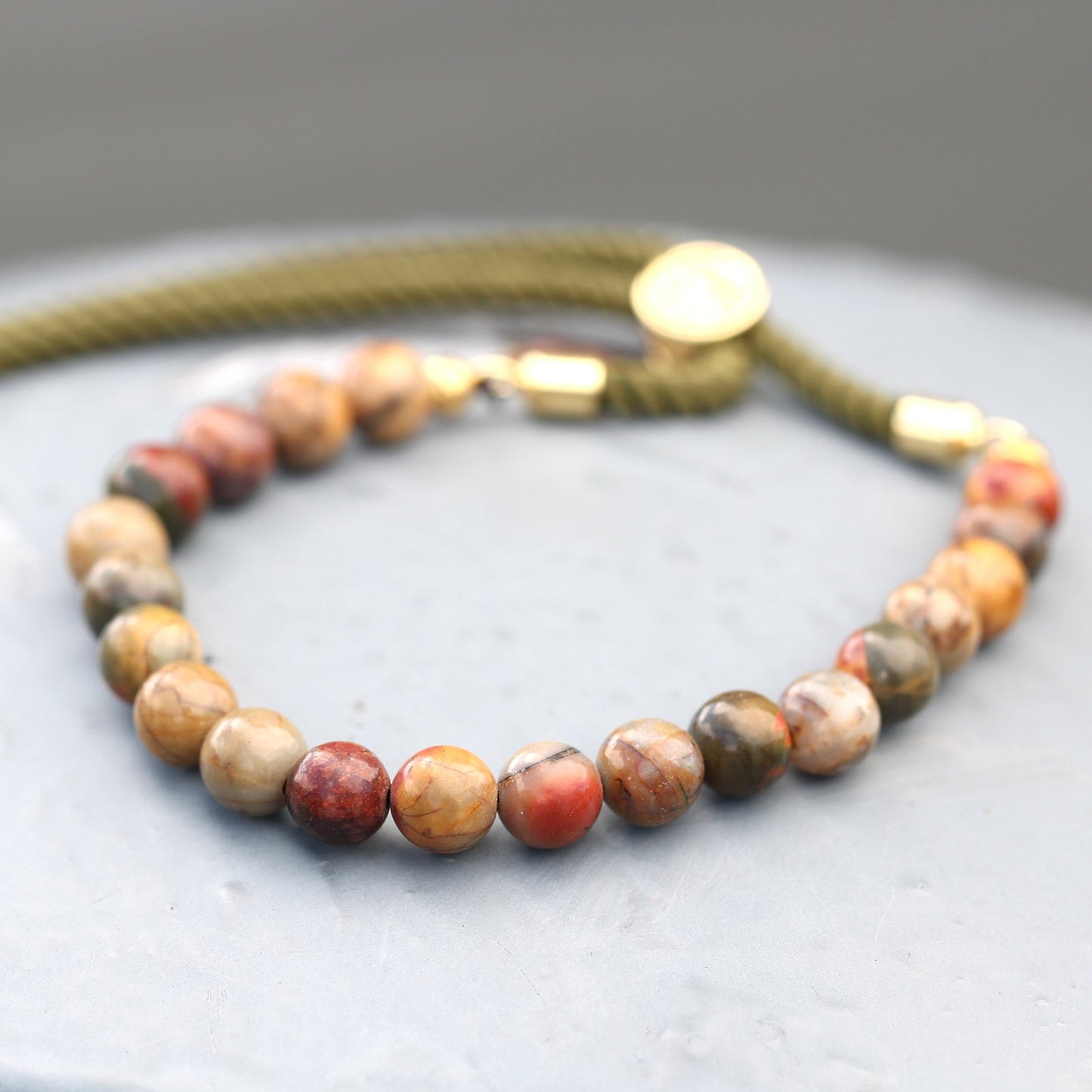 Unisex Handcrafted 18K Gold Plated Gemstone Bracelet - Moss Green String / Picasso Jasper product packaging on clean background from Quintessential Holistic Health Ltd