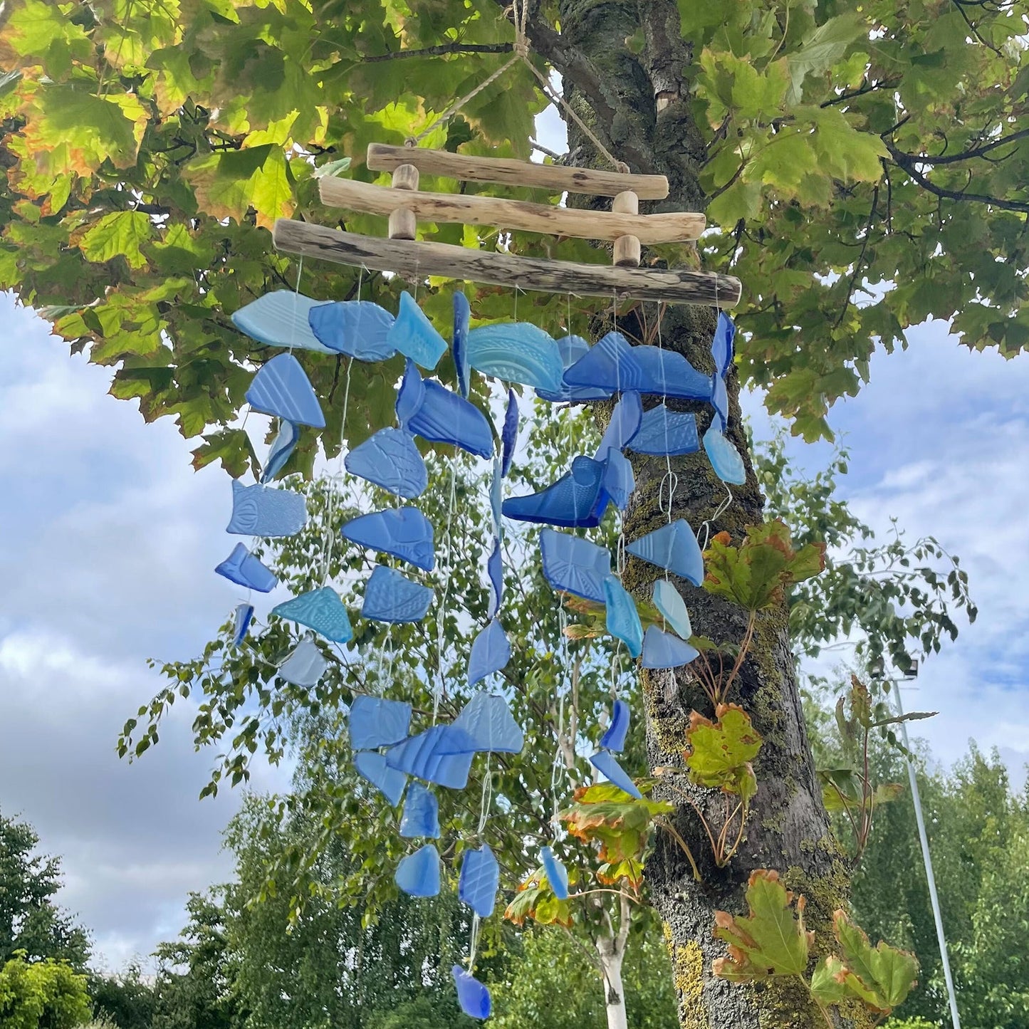 Driftwood & Recycled Glass Wind Chime - Three-Stick Blue, vivid blue glass strands suspended from driftwood bars outdoors by Quintessential Holistic Health Ltd