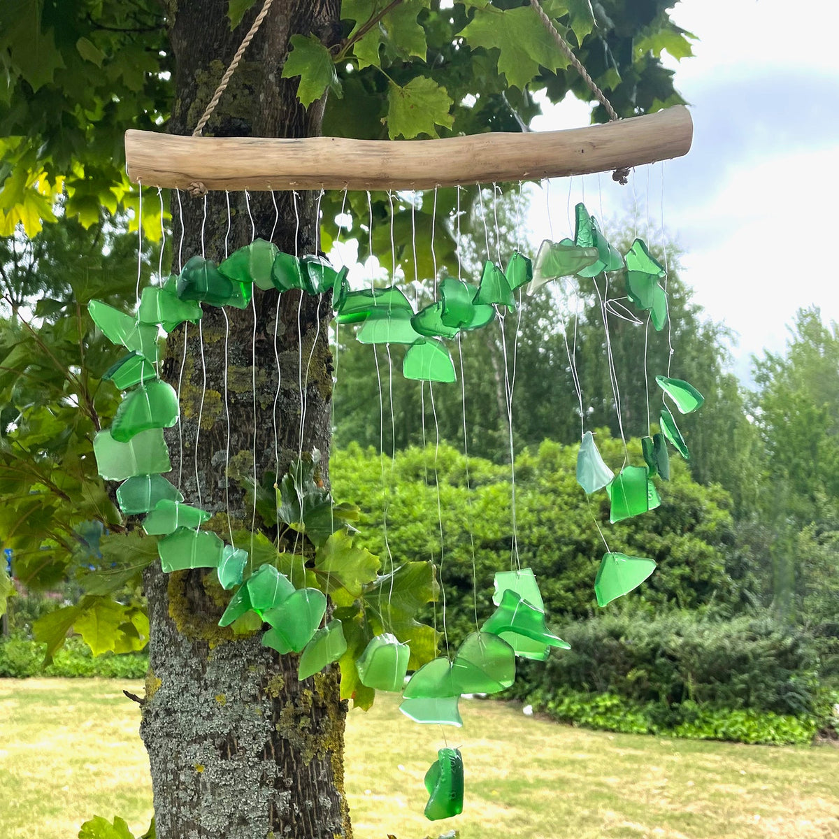 Recycled Glass & Driftwood Wind Chime - Green Loving Heart hanging from a tree with green glass pieces and dangling strands by Quintessential Holistic Health Ltd