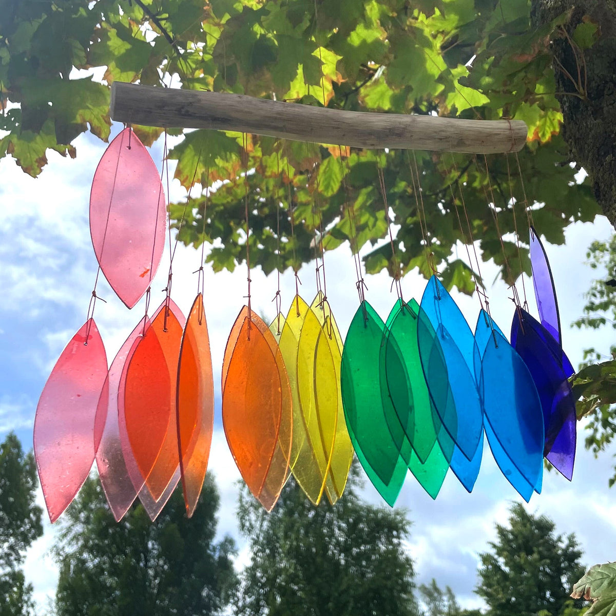 Driftwood and Recycled Glass Wind Chime - Rainbow - Multicoloured with overlapping curved pieces hanging outdoors beneath driftwood by Quintessential Holistic Health Ltd