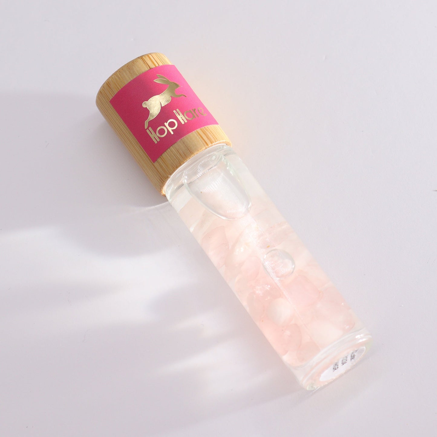 Gemstone Tarot Essential Oil Roll-On - Rose Quartz - The Lovers with a clear bottle of pale pink chips lying diagonally by Quintessential Holistic Health Ltd