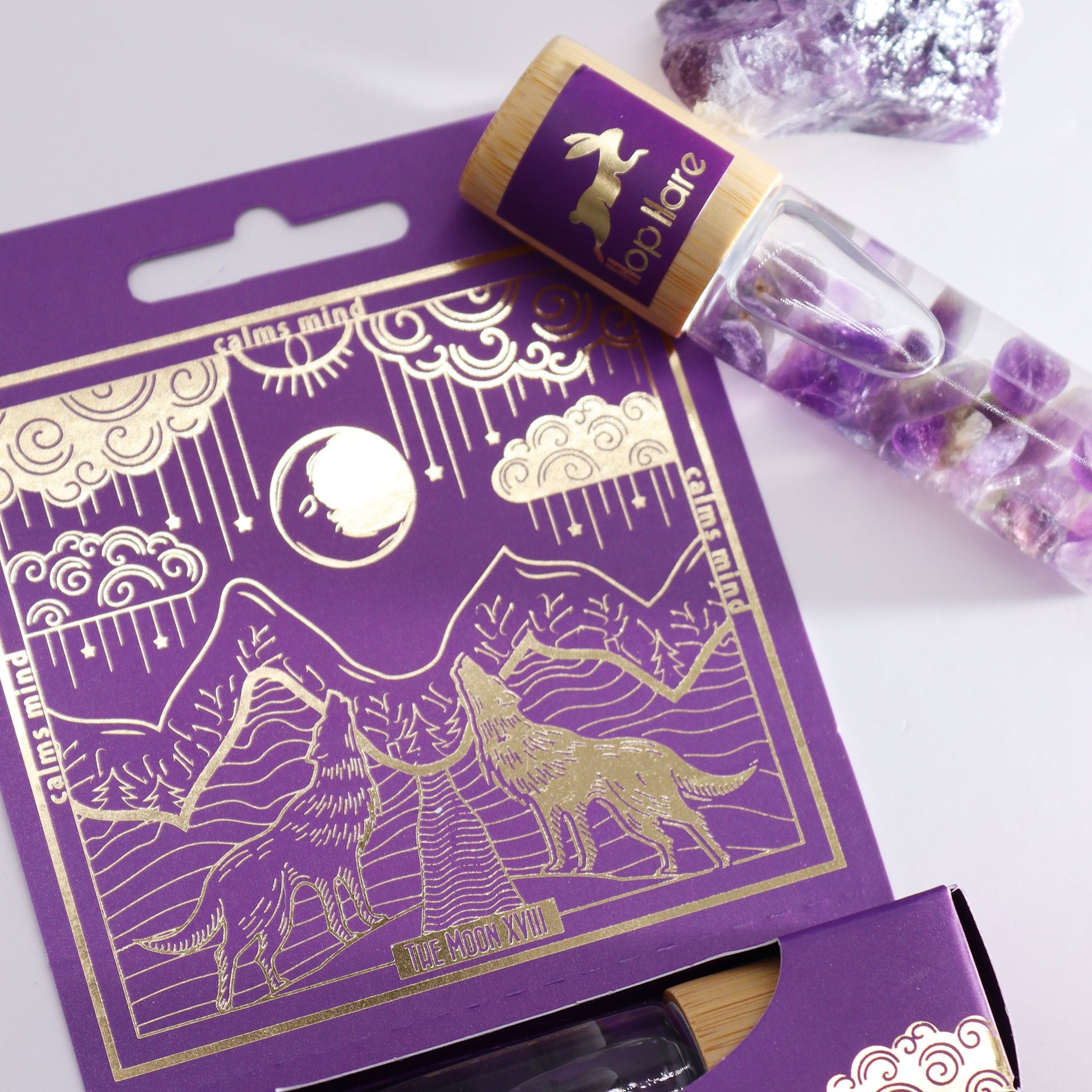 Gemstone Tarot Essential Oil Roll-On - Amethyst - The Moon with bottle resting across the purple mountain-illustrated box by Quintessential Holistic Health Ltd