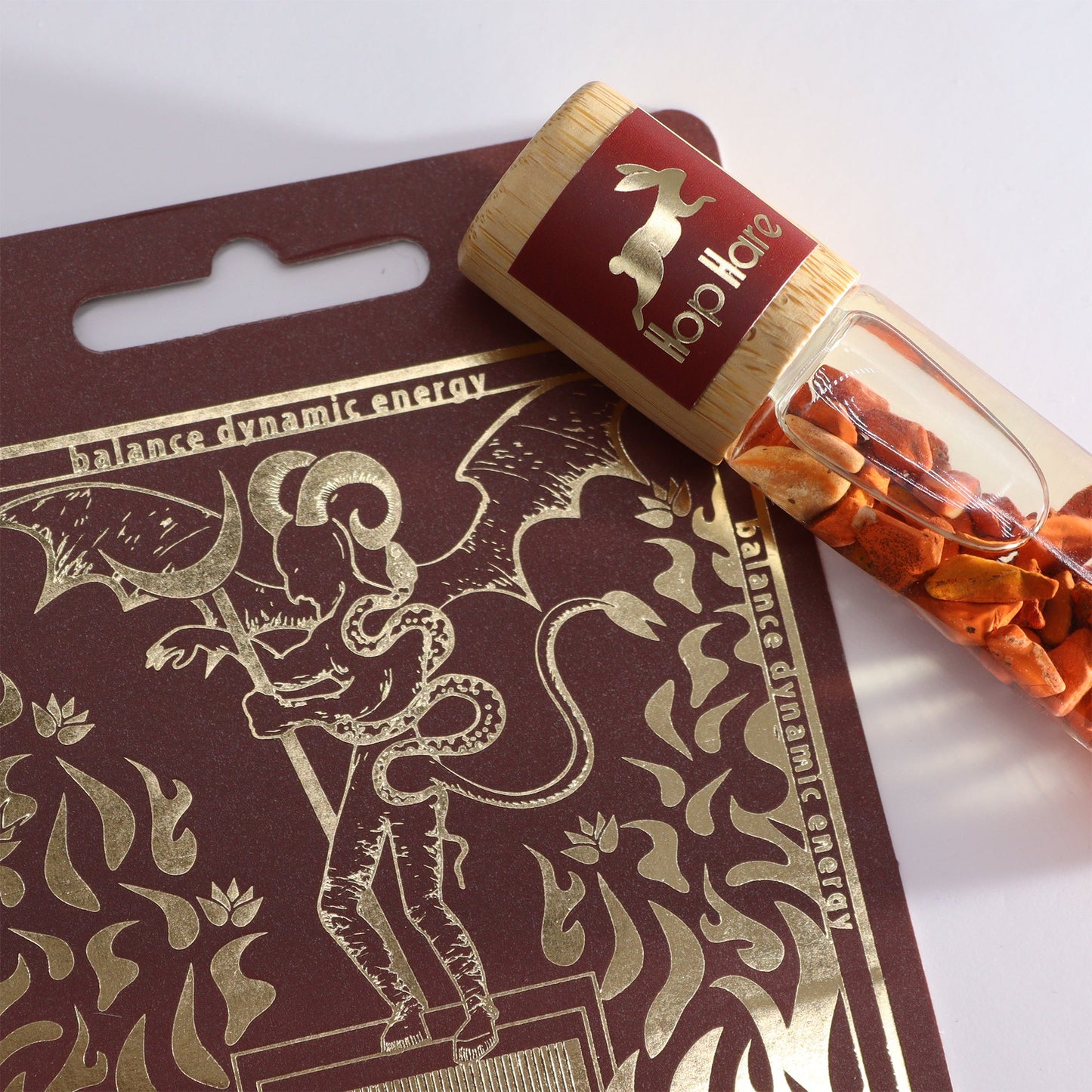 Gemstone Tarot Essential Oil Roll-On - Red Jasper - The Devil with orange chips in a bottle resting on the illustrated box by Quintessential Holistic Health Ltd
