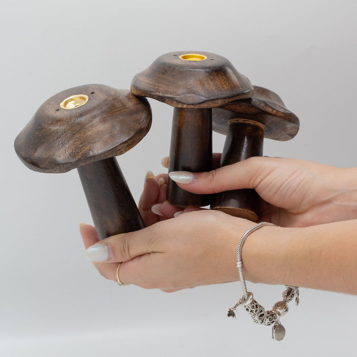 Set of 3 Mango Wood Incense Holders - Flat Mushrooms, three dark brown mushroom-shaped pieces displayed in two hands by Quintessential Holistic Health Ltd