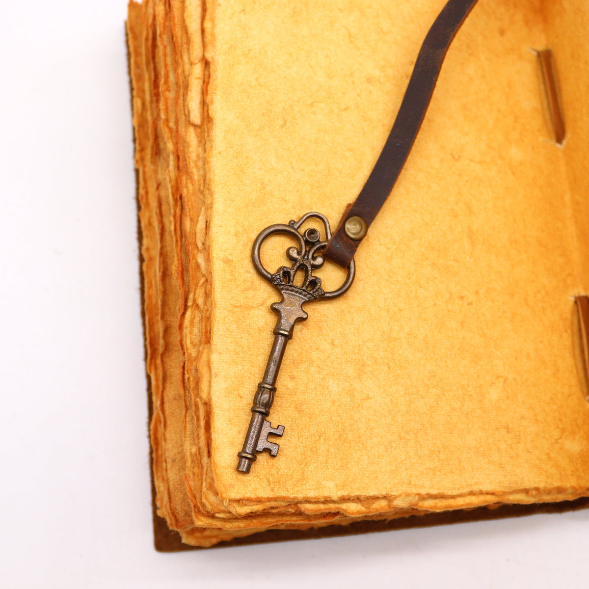 Oiled Leather 200-Page Deckle-Edged Notebook – Medium Brown shown open with a metal key charm resting on a tan page by Quintessential Holistic Health Ltd