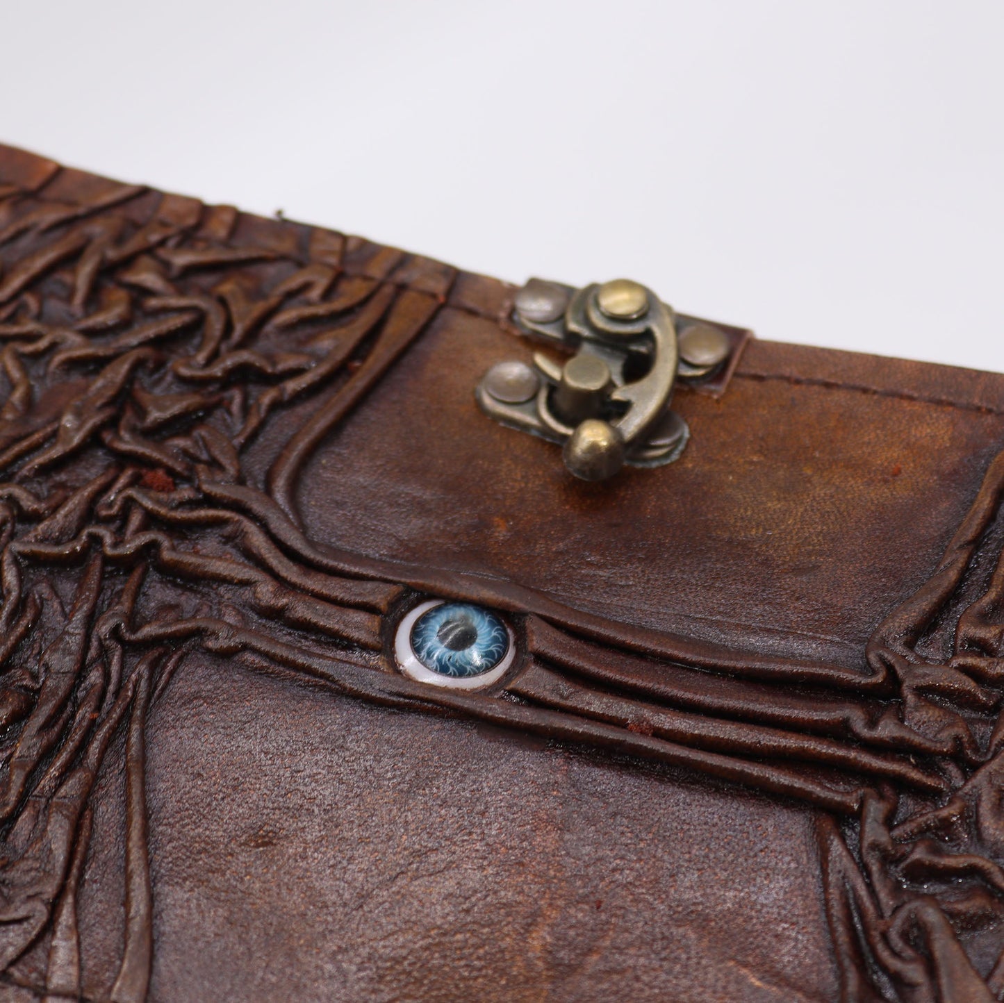 Medium Brown Leather-Bound Notebook - Evil Eye, Clasp & Deckle Edges, close view of the blue eye, embossed branches and clasp by Quintessential Holistic Health Ltd