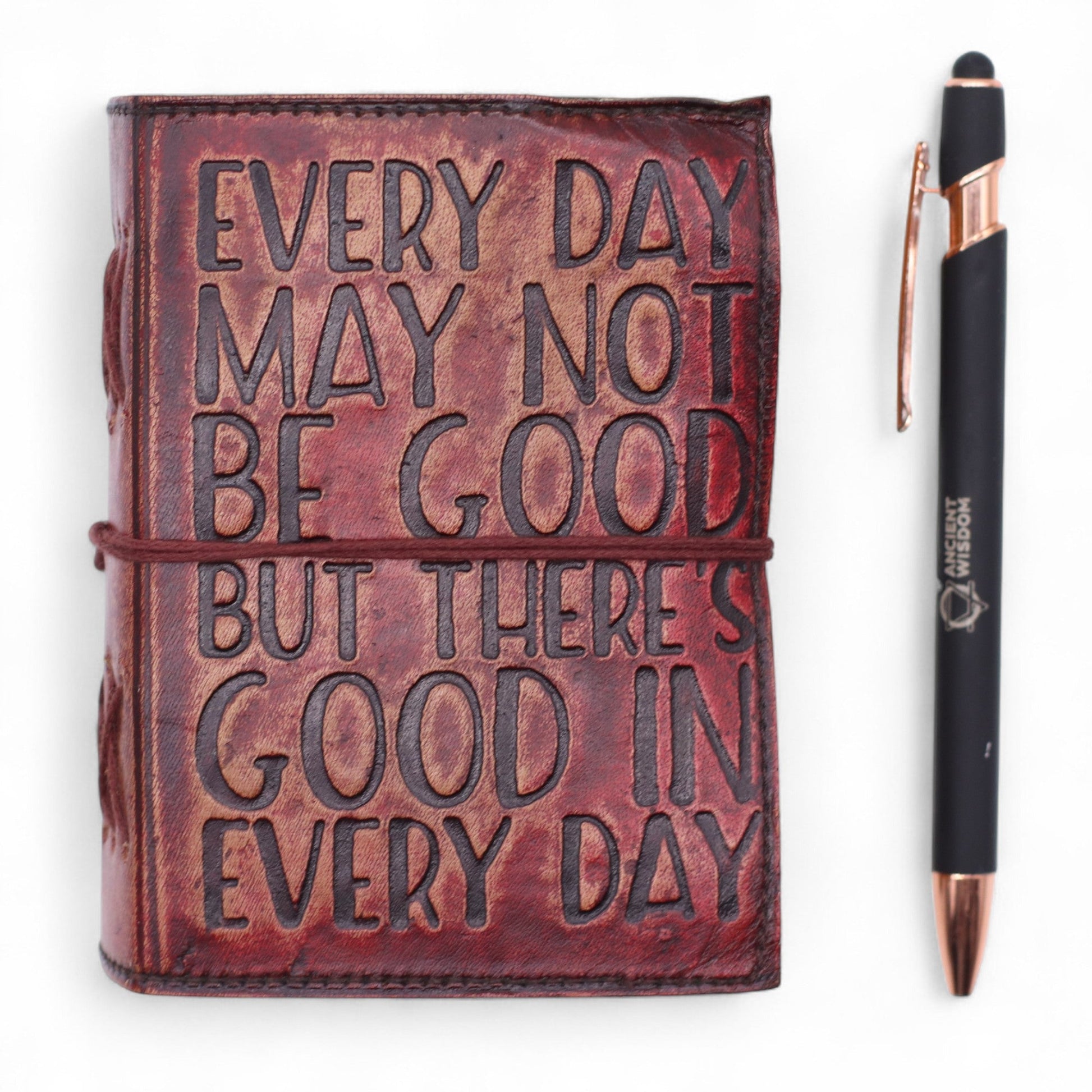 Small Brown Deckle-Edged Leather Wrap Journal - Good in Every Day with a reddish-brown lettered cover beside a black pen by Quintessential Holistic Health Ltd