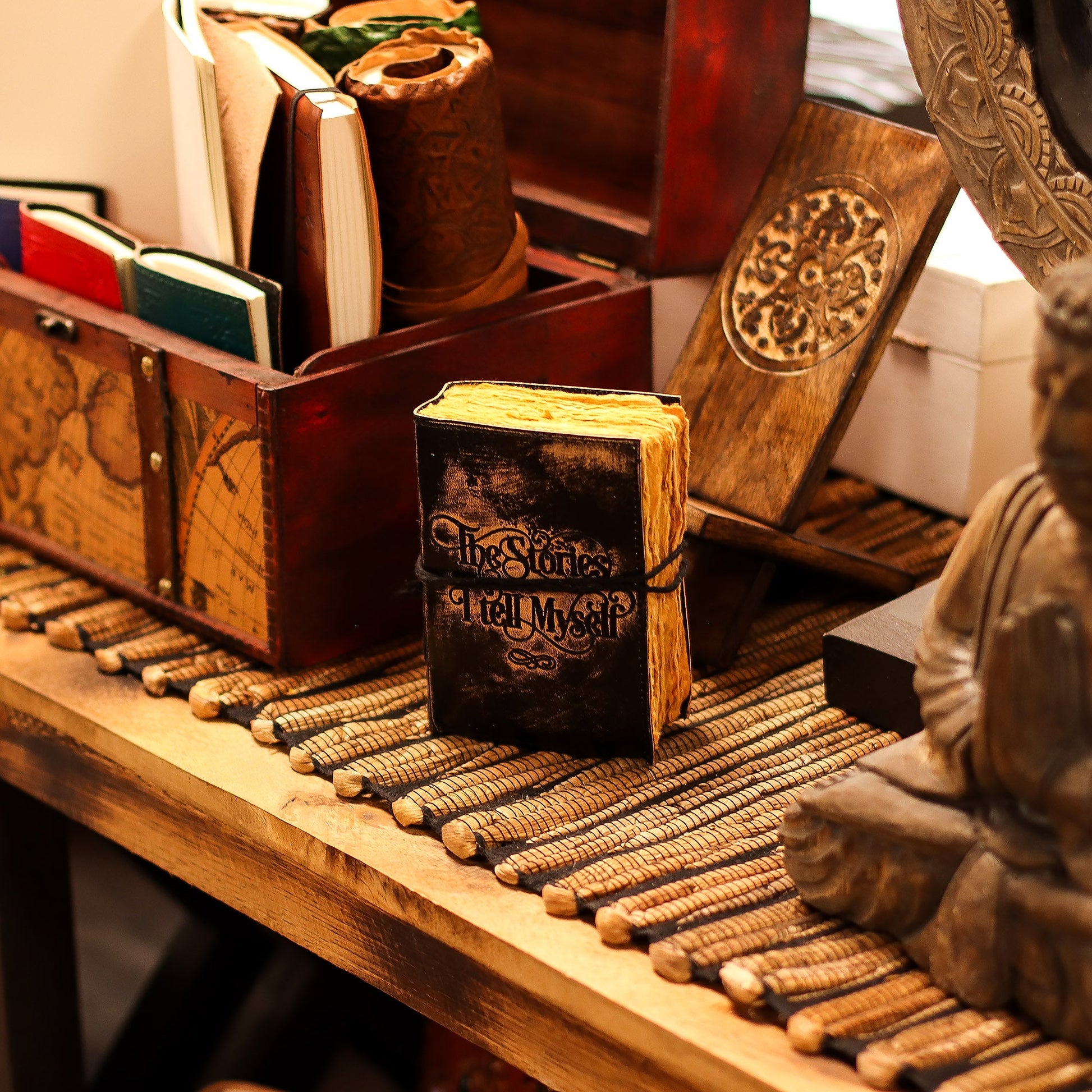 Small Black and Tan Leather Journal - The Stories I Tell Myself, standing closed among desk accessories with its embossed cover visible by Quintessential Holistic Health Ltd