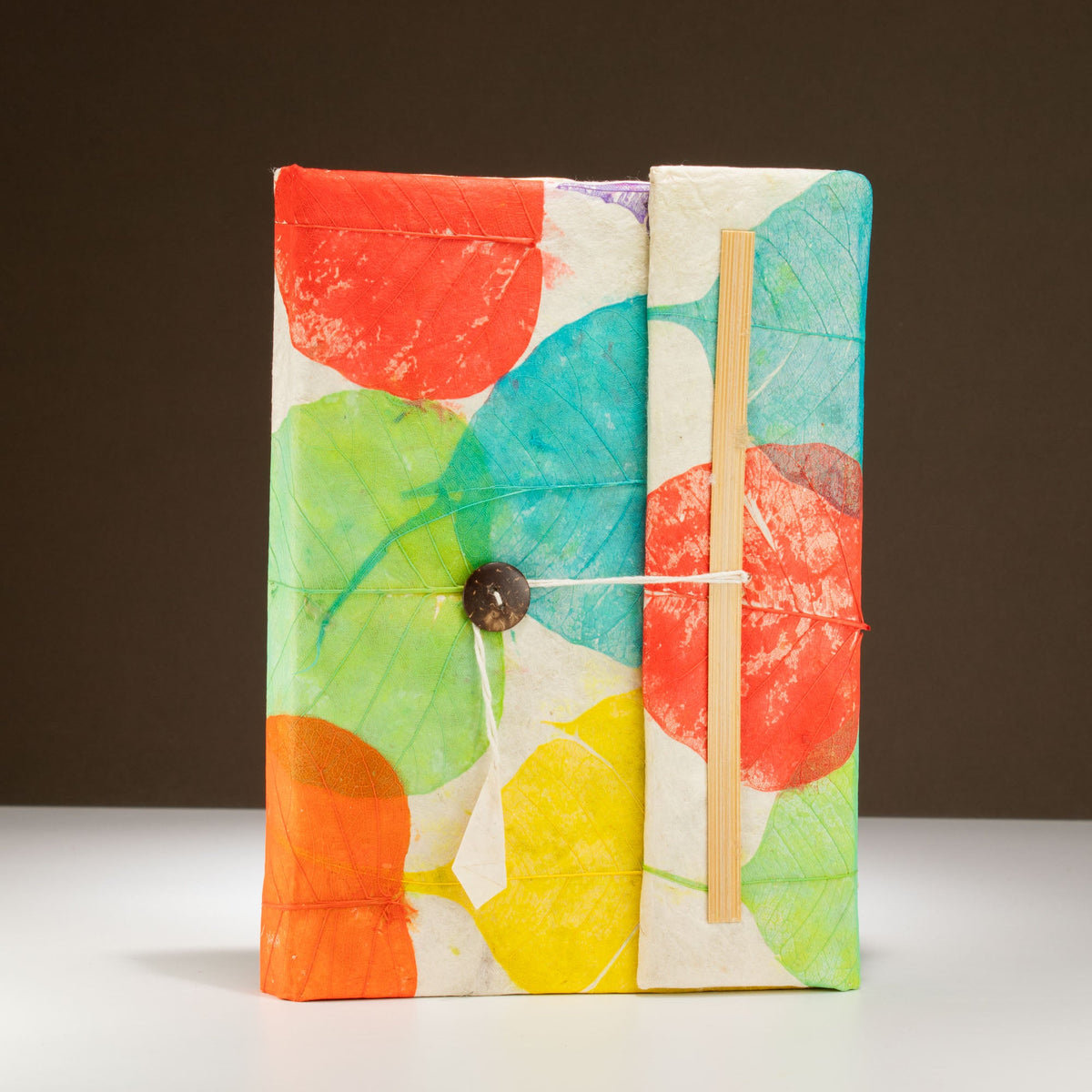 Eco-Friendly Lokta Paper Notebook - A5 - Colourful Leaves with bright overlapping shapes, a dark button and white cord by Quintessential Holistic Health Ltd