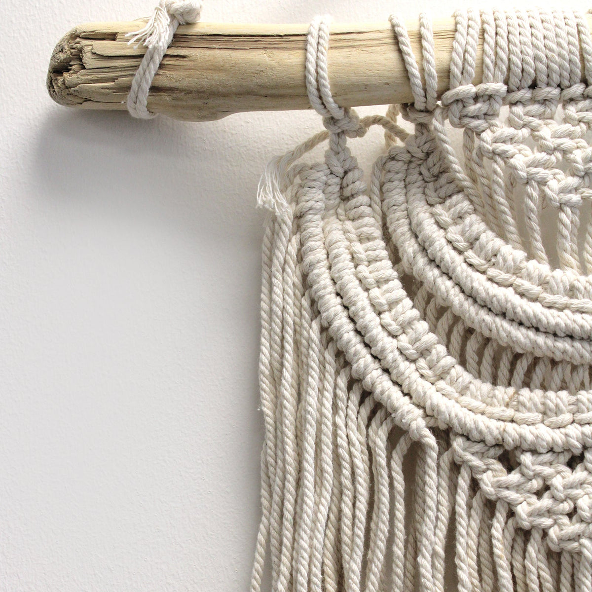 Handcrafted Cotton Macramé Wall Hanging - Two Waves showing sweeping knotted arcs and hanging cords attached to a wooden branch by Quintessential Holistic Health Ltd