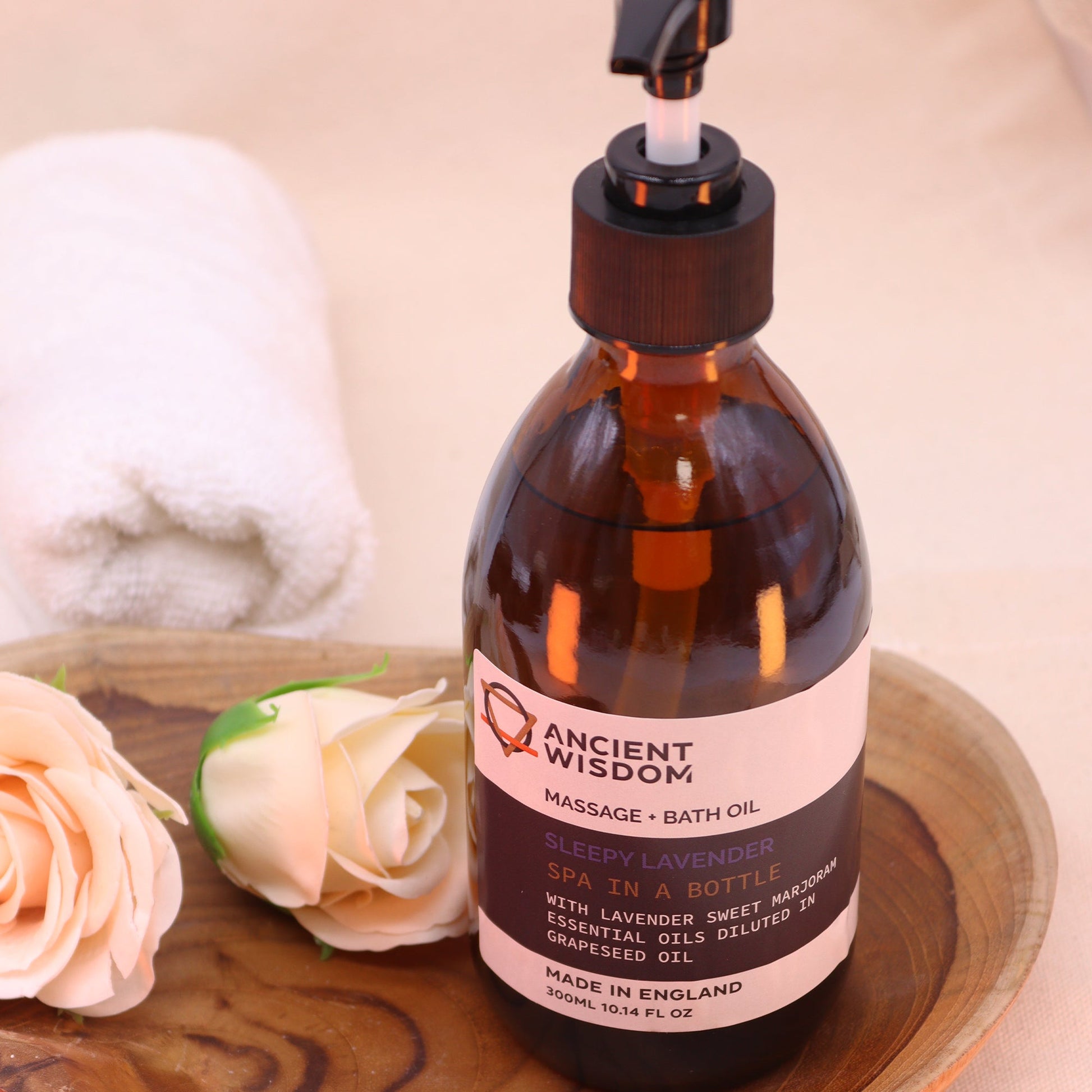 Sleepy Lavender 300ml Aromatherapy Massage & Bath Oil with Pump standing beside folded towels and pale roses by Quintessential Holistic Health Ltd