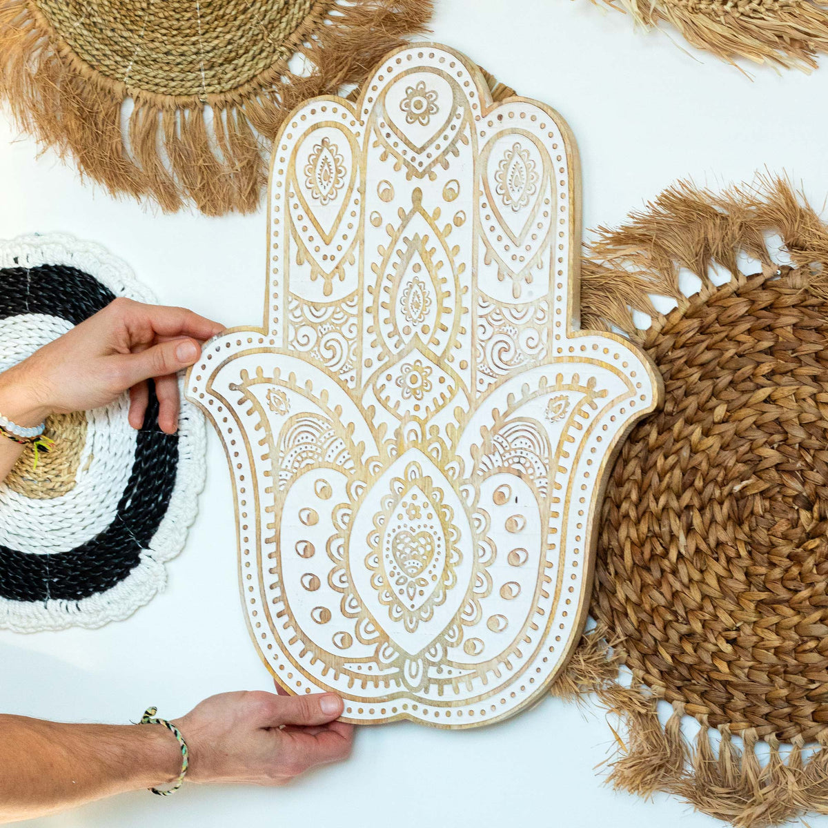Hand-Carved Mango Wood Hamsa Wall Plaque - Whitewash, held upright in two hands with its carved face visible, by Quintessential Holistic Health Ltd