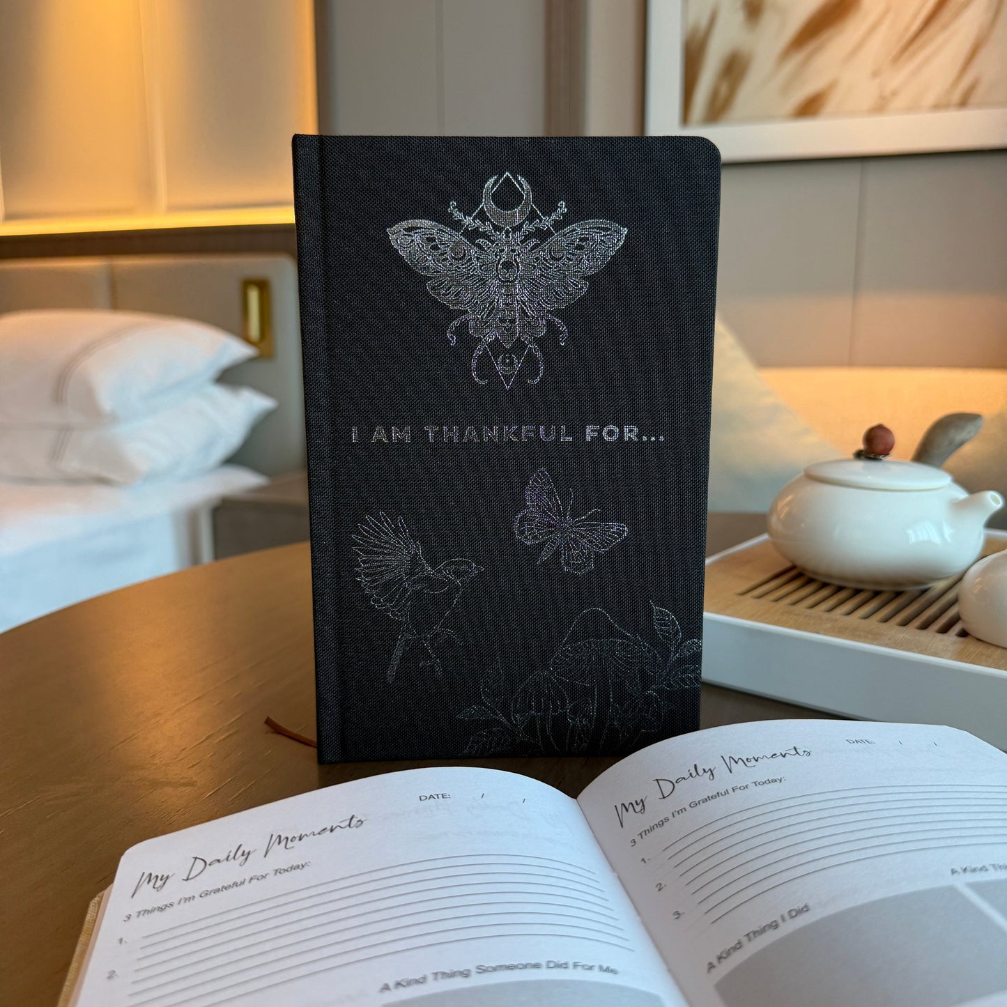 Gratitude Journal with Silver - A5 - Black - I am Thankful, standing closed behind an open guided journal by Quintessential Holistic Health Ltd