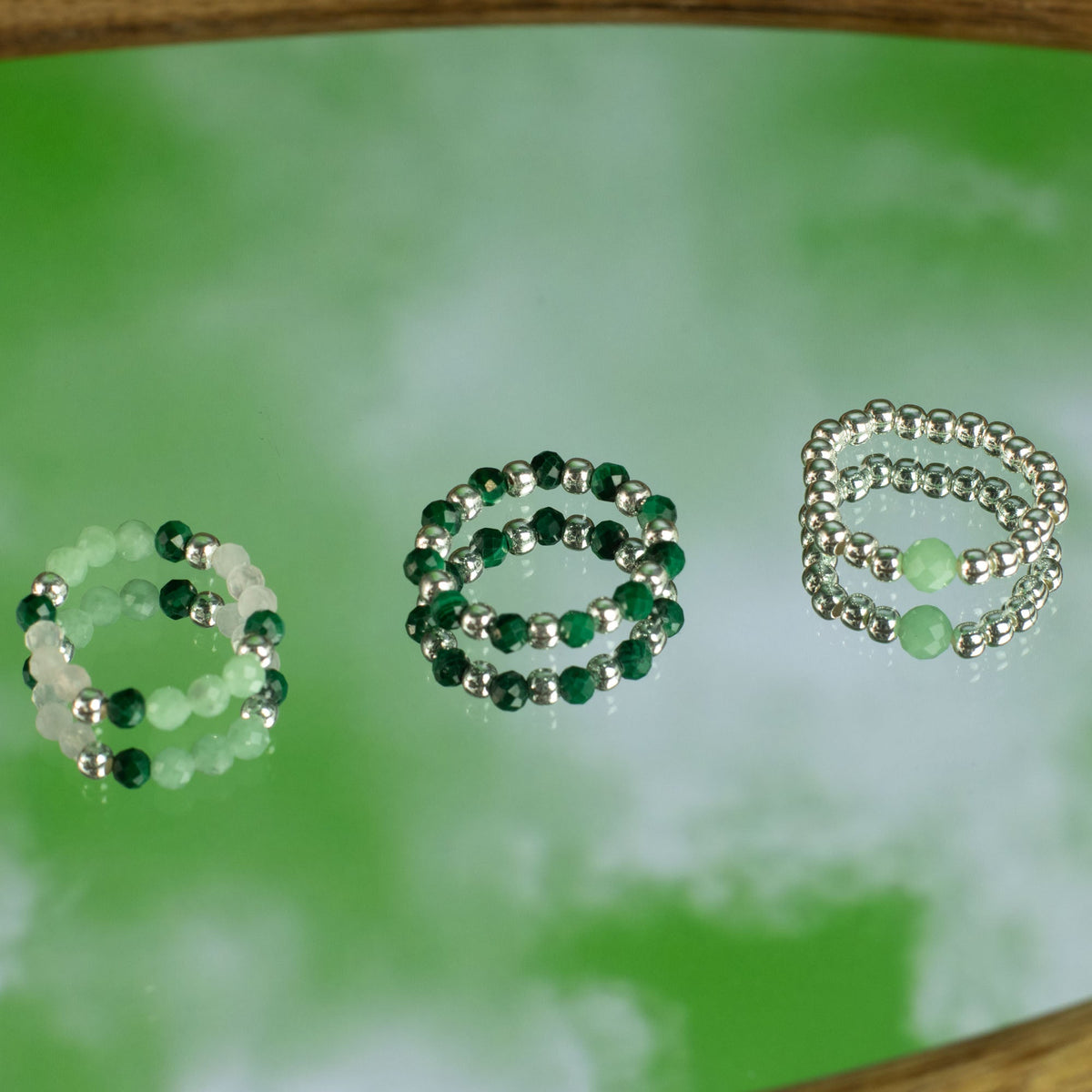 Mystical Nymph Spirit Gemstone 3-Ring Set – Forest Spirit, three beaded rings arranged separately on a reflective green surface by Quintessential Holistic Health Ltd