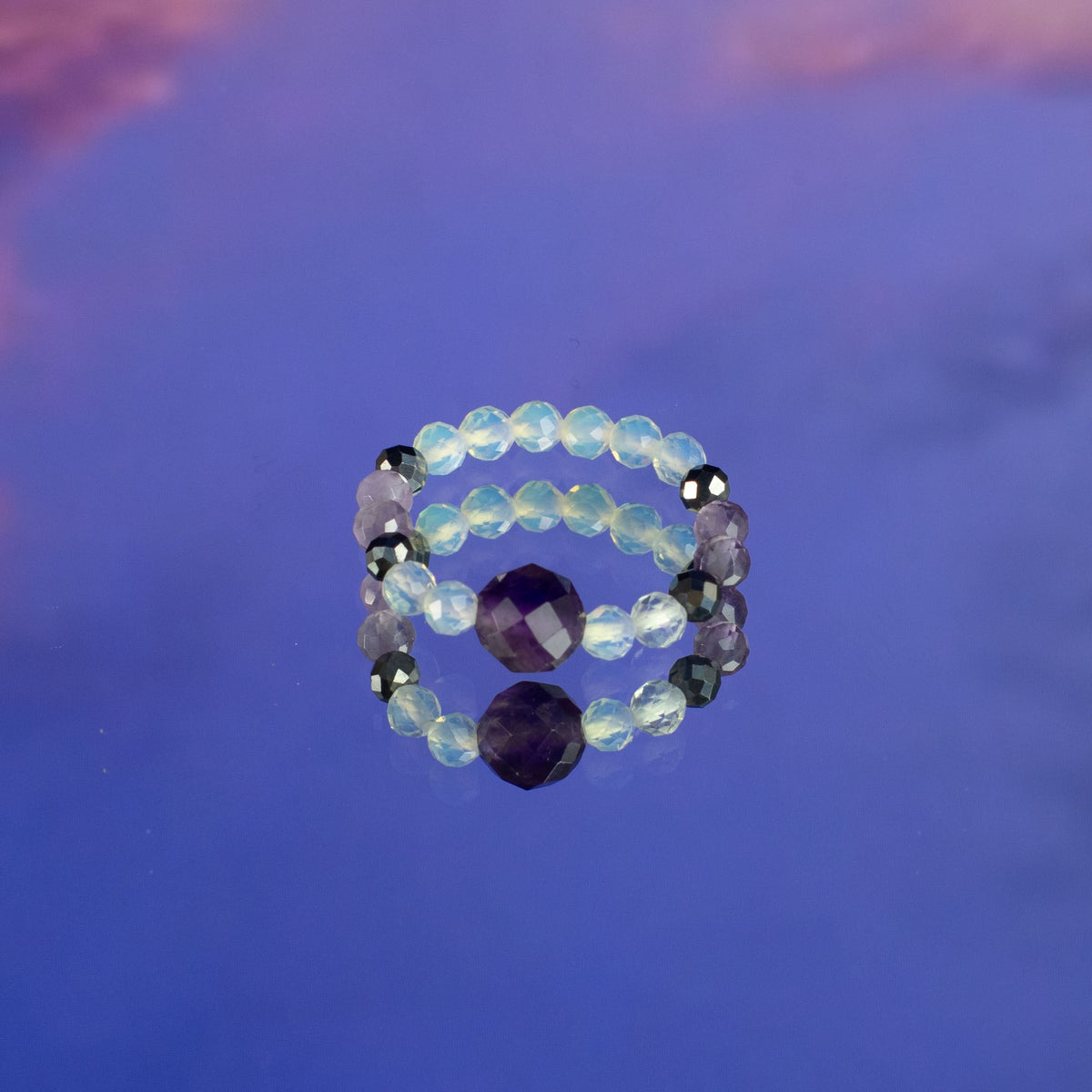 Mystical Nymph Spirit Gemstone 3-Ring Set – Full Moon, pale blue and purple beaded rings stacked around a large purple bead against blue, by Quintessential Holistic Health Ltd
