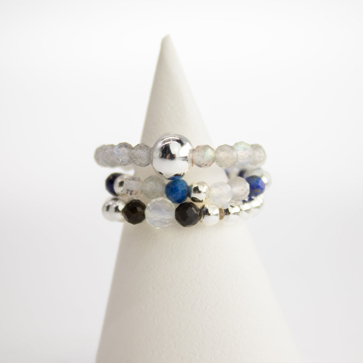 Mystical Nymph Spirit Gemstone 3-Ring Set – Northern Lights stacked on a white cone with pale blue, dark blue and silver-tone beads by Quintessential Holistic Health Ltd