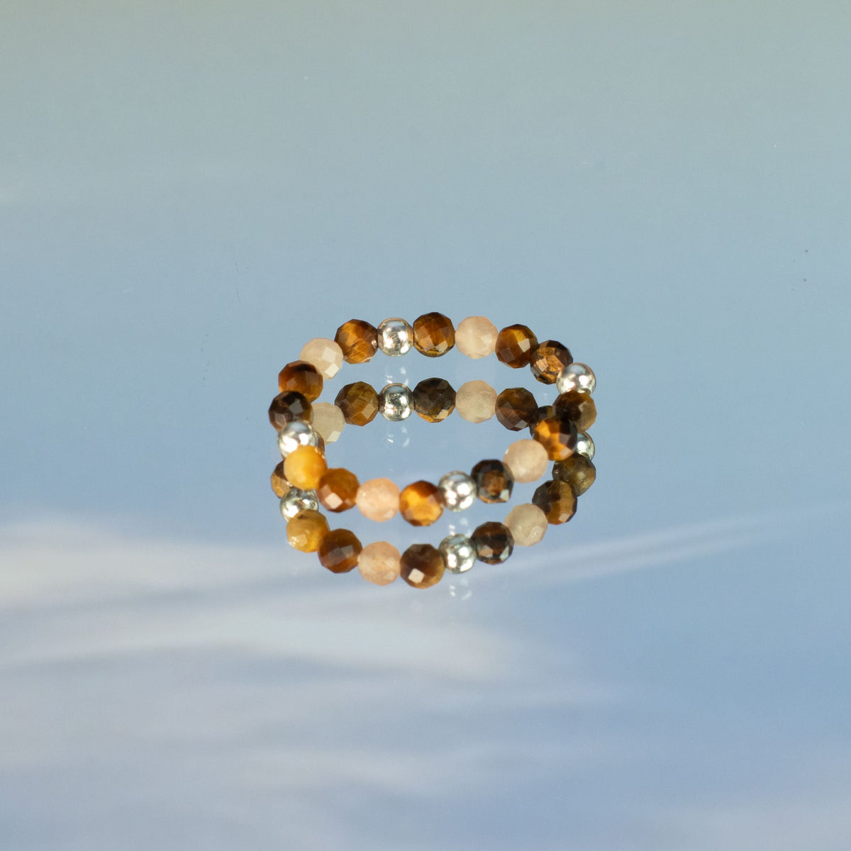 Mystical Nymph Spirit Gemstone 3-Ring Set – Sea Sunset showing a brown, peach and white beaded ring on a reflective pale blue surface by Quintessential Holistic Health Ltd
