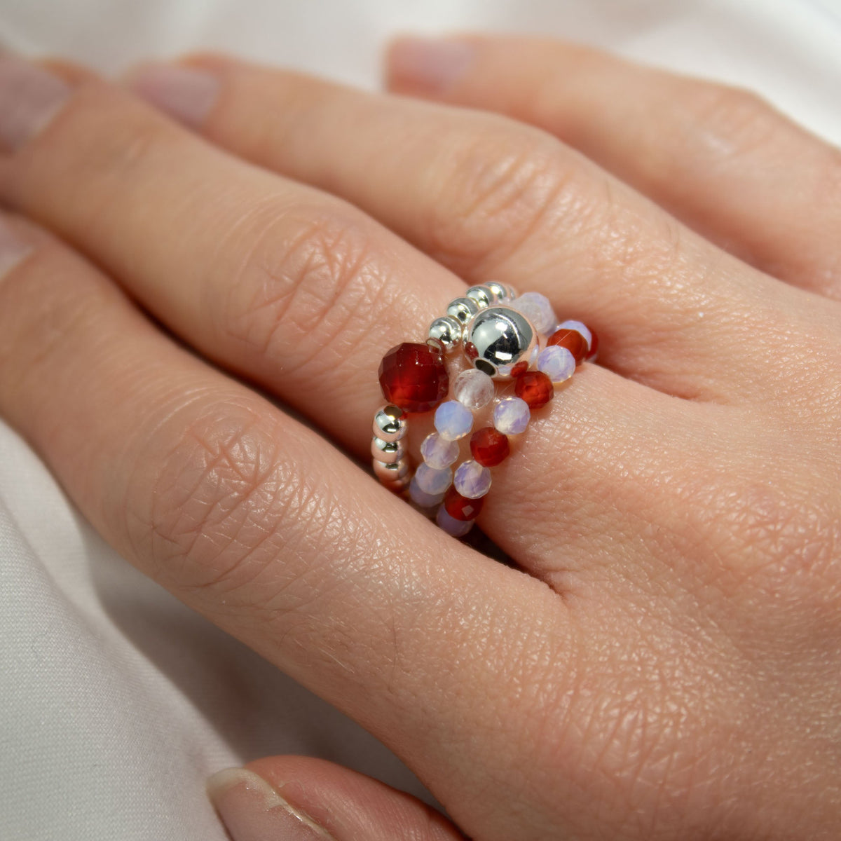 Mystical Nymph Spirit Gemstone 3-Ring Set – Blood Moon, red, pale and silver-toned beaded rings worn stacked on a hand by Quintessential Holistic Health Ltd