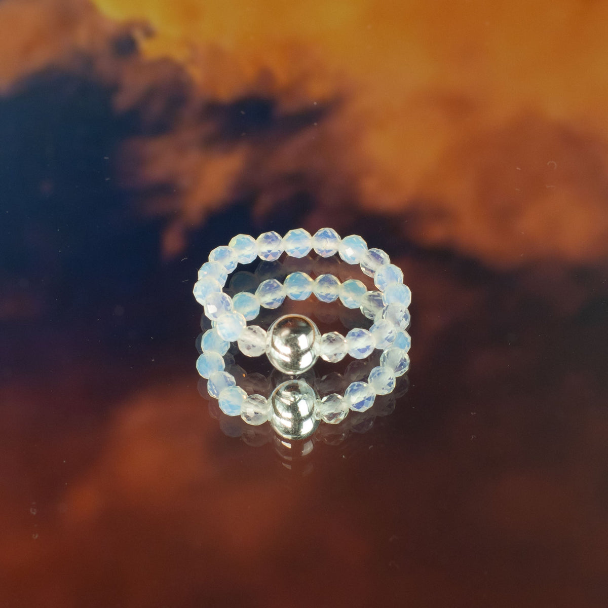 Mystical Nymph Spirit Gemstone 3-Ring Set – Blood Moon, pale beaded rings stacked with silver-toned accents on reflective amber by Quintessential Holistic Health Ltd