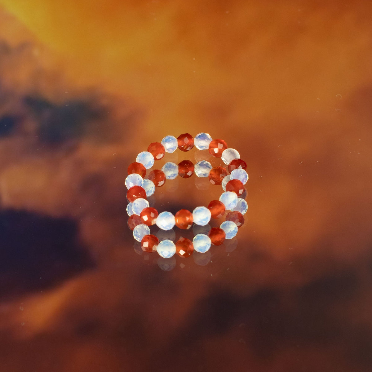 Mystical Nymph Spirit Gemstone 3-Ring Set – Blood Moon, red and pale beaded rings stacked on a reflective amber surface by Quintessential Holistic Health Ltd