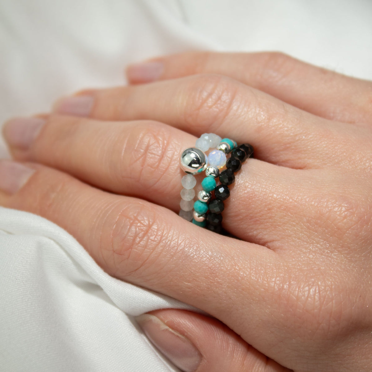 Mystical Nymph Spirit Gemstone 3-Ring Set – Endless Ocean, turquoise, dark and pale beaded rings worn stacked on a hand by Quintessential Holistic Health Ltd