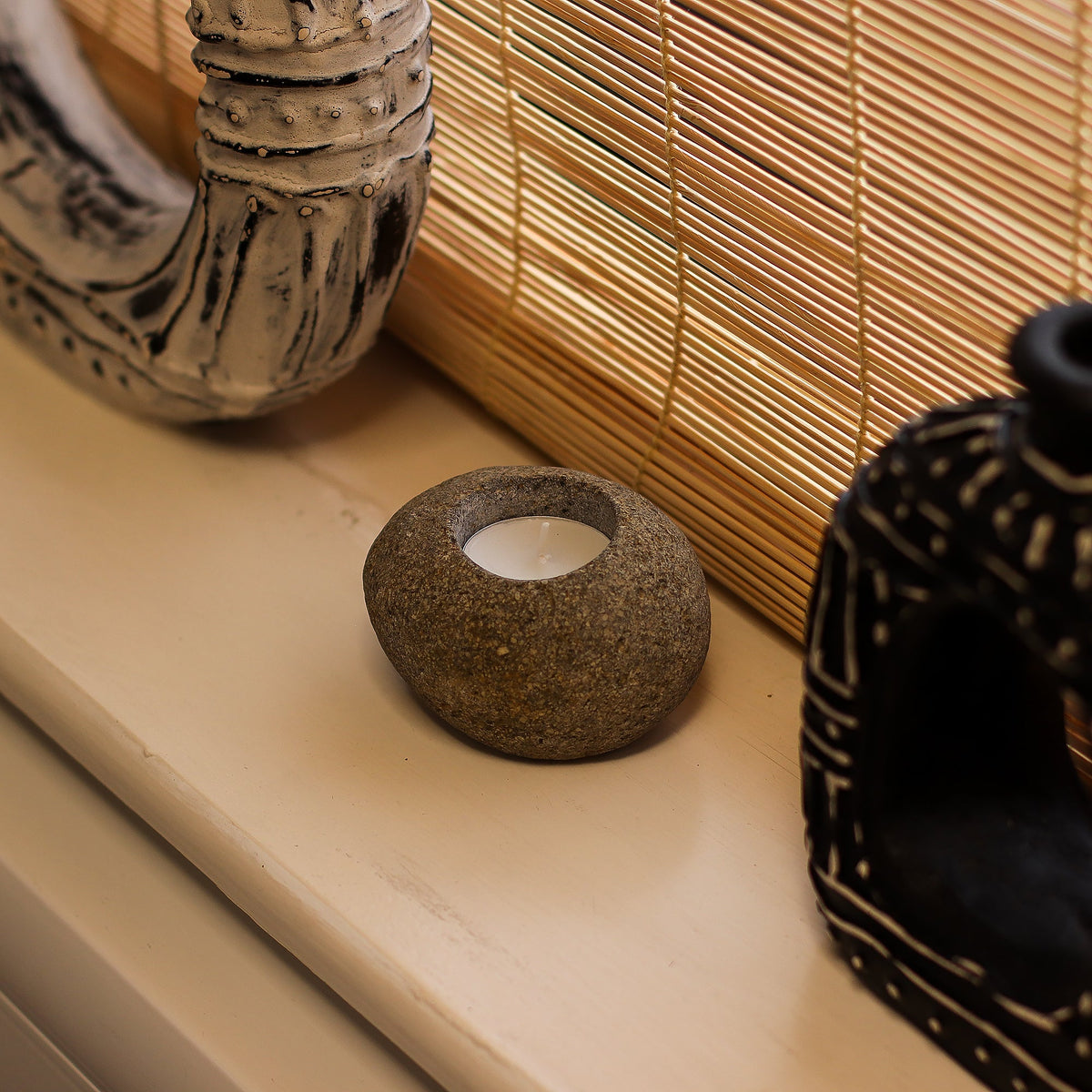 Natural Riverstone Tea Light Candle Holder - Single, small rounded brown stone with one white tea light beside decorative objects by Quintessential Holistic Health Ltd