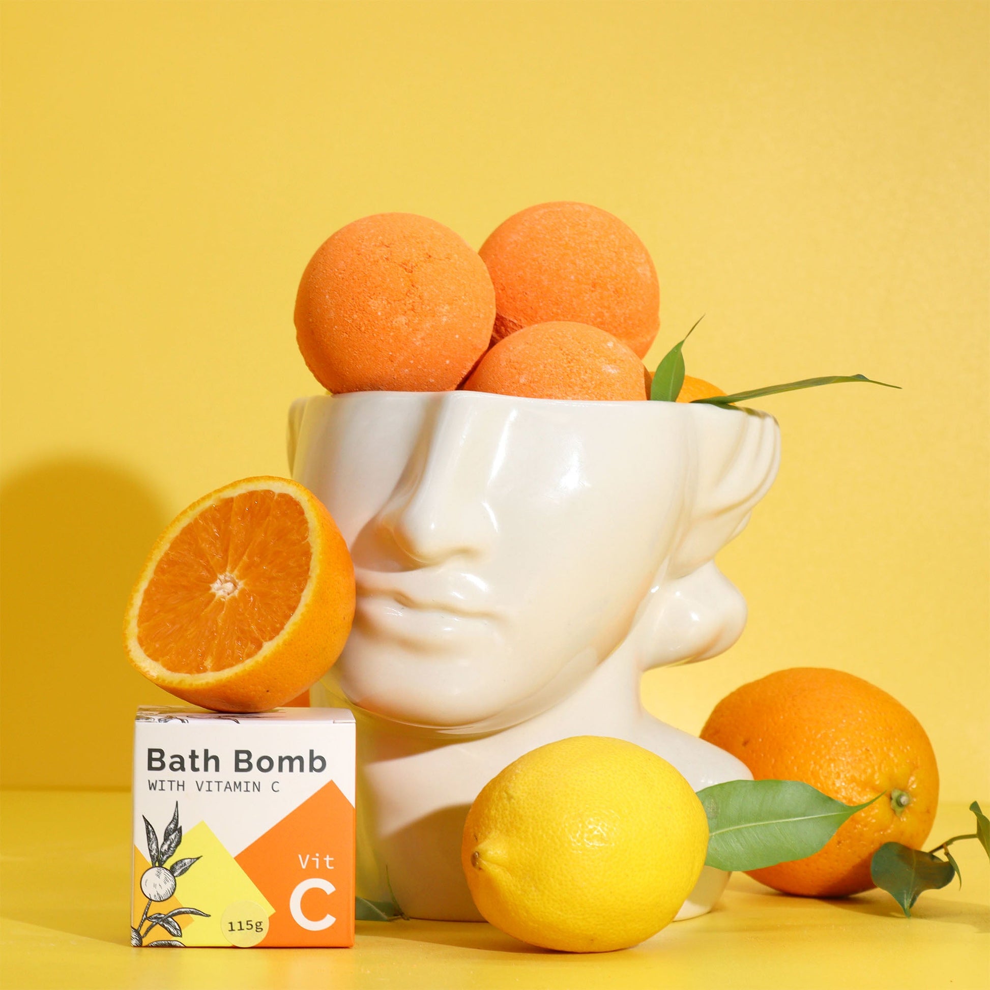 Vitamin C-Infused Bath Bomb with Essential Oils, boxed bath bomb displayed with oranges, lemons and a white face sculpture, by Quintessential Holistic Health Ltd