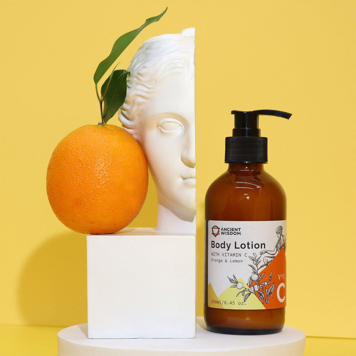 Vitamin C Goddess’s Body Lotion - Orange and Lemon, amber pump bottle displayed with an orange and white face sculpture, by Quintessential Holistic Health Ltd
