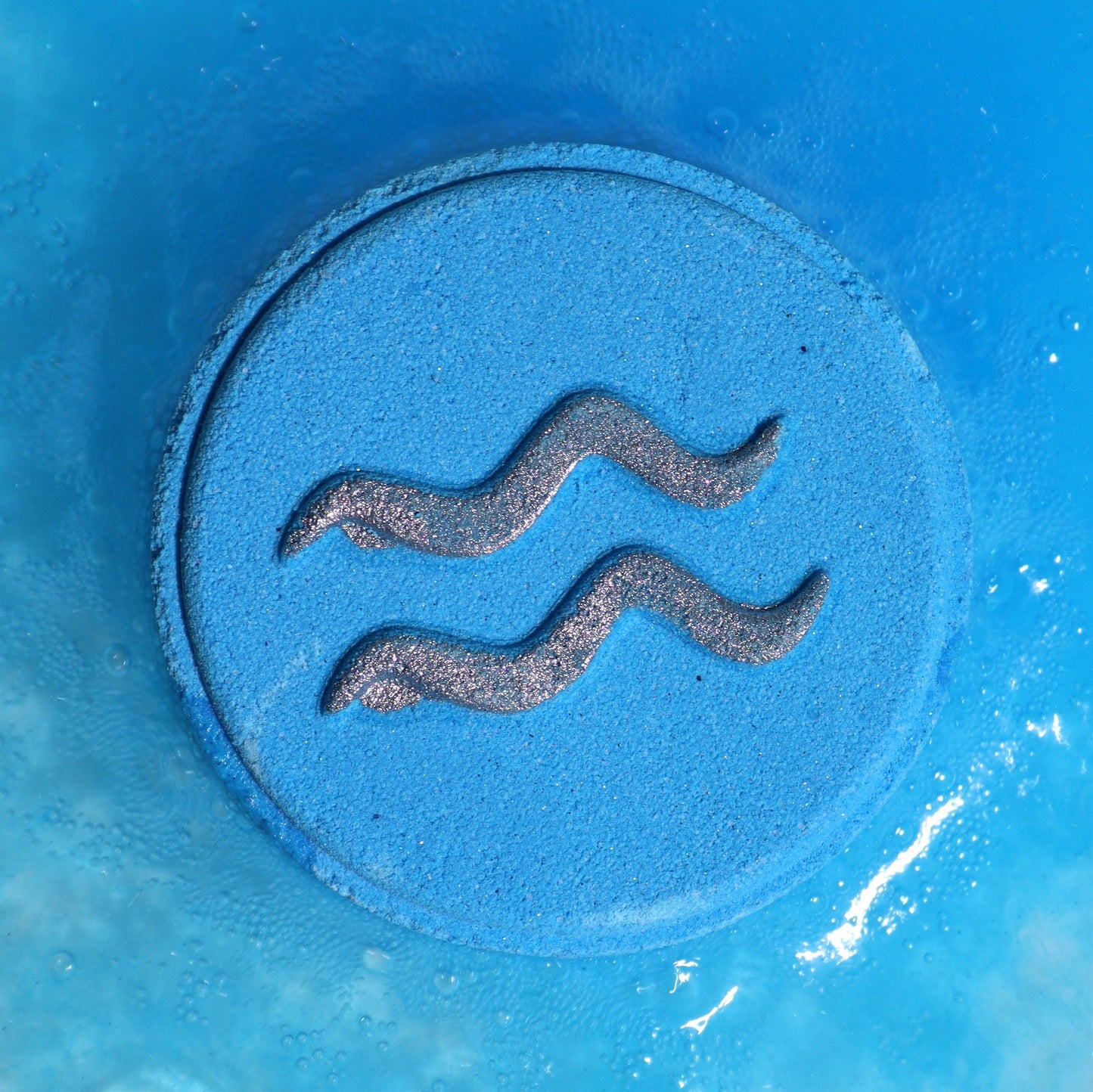 Aquarius Bath Bomb Fizzers - Amethyst Crystal & Amber - 2 Pack, close-up of a blue round fizzer embossed with wavy lines by Quintessential Holistic Health Ltd