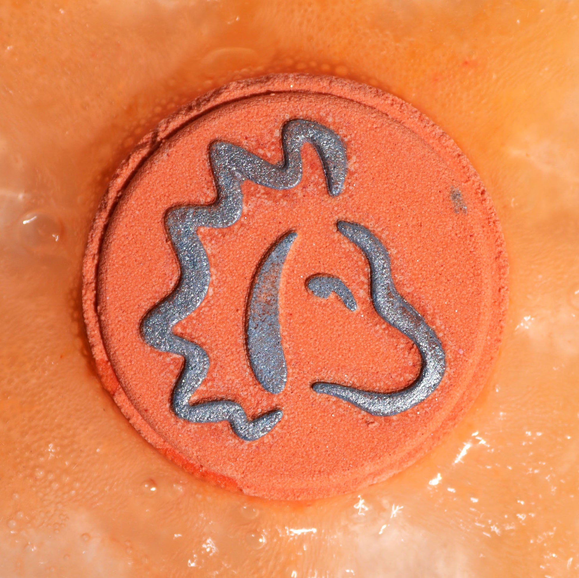 Leo Bath Bomb Fizzers - Frosted Citrine & Ginger - 2 Pack, close-up of an orange round fizzer embossed with the Leo symbol by Quintessential Holistic Health Ltd