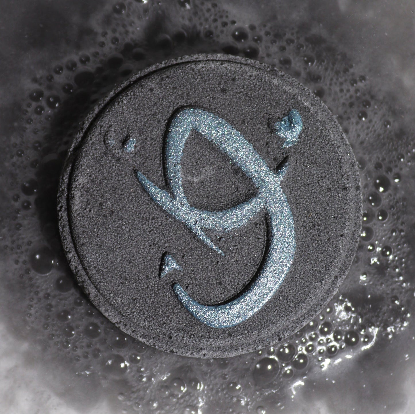 Scorpio Zodiac Bath Bomb Fizzers - Obsidian & Dark Coffee - 2 Pack, close-up of a dark grey fizzer embossed with the Scorpio symbol by Quintessential Holistic Health Ltd